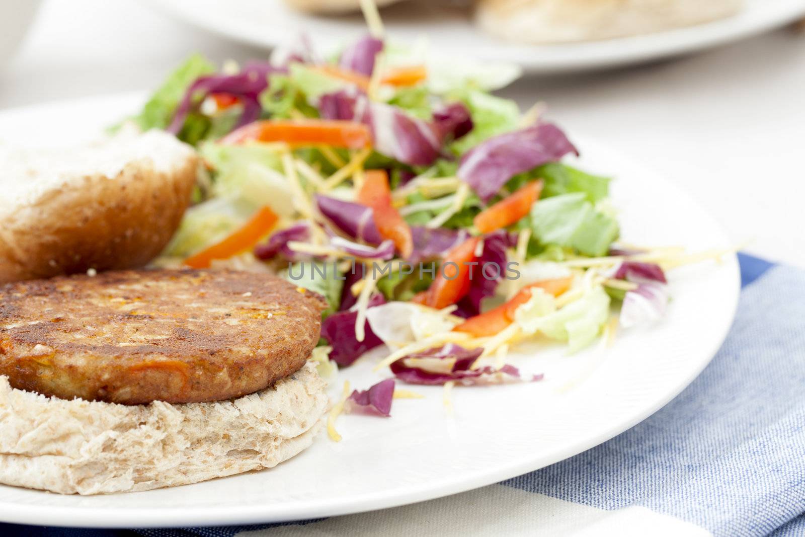 Veggie burger pattie on a bun with a fresh green salad.