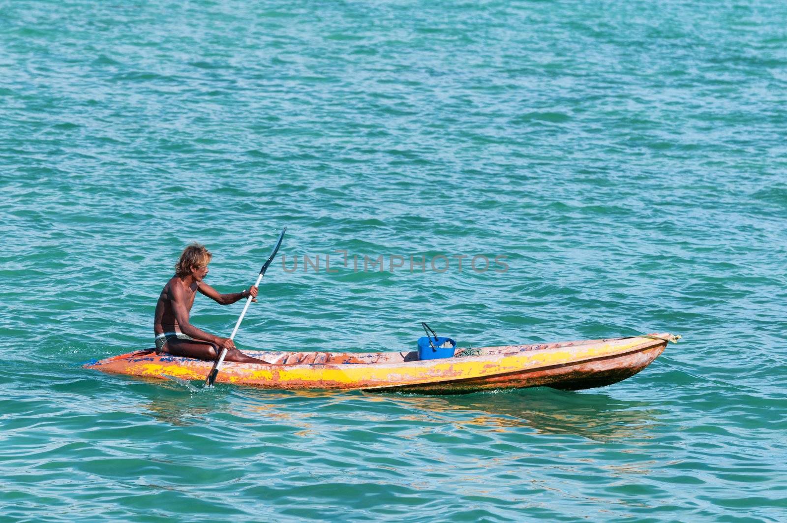 Phuket, Thailand - January 19, 2012: Bronzed Thai fisherman on small boat rows across blue sea
