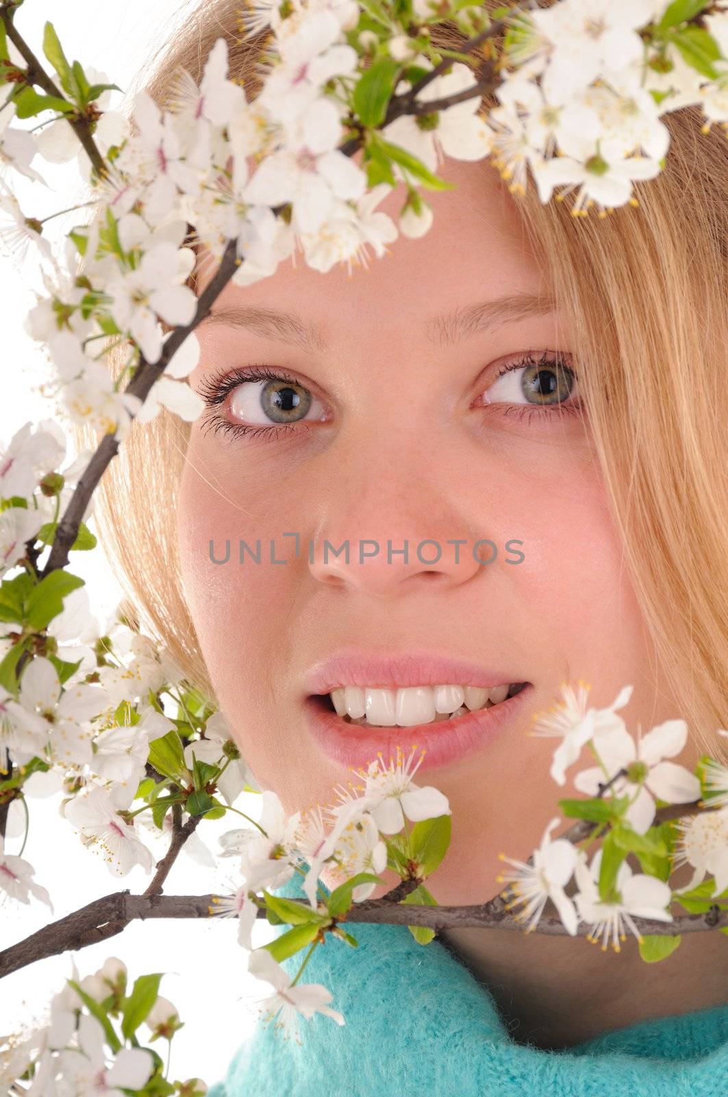 Smiling blonde woman behind spring white cherry flowers. Focus on woman's eyes.