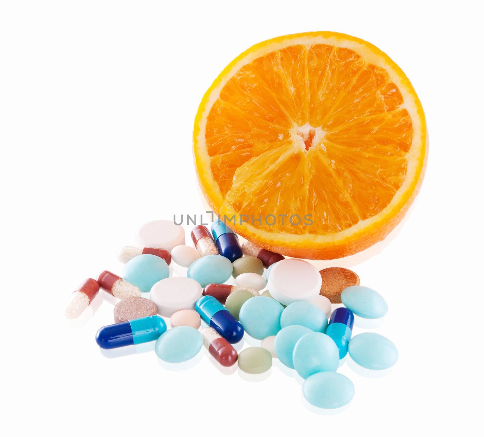 Concept of tasty madicine with heap of pills in front of one orange slice with reflection on white background. Focus on orange.