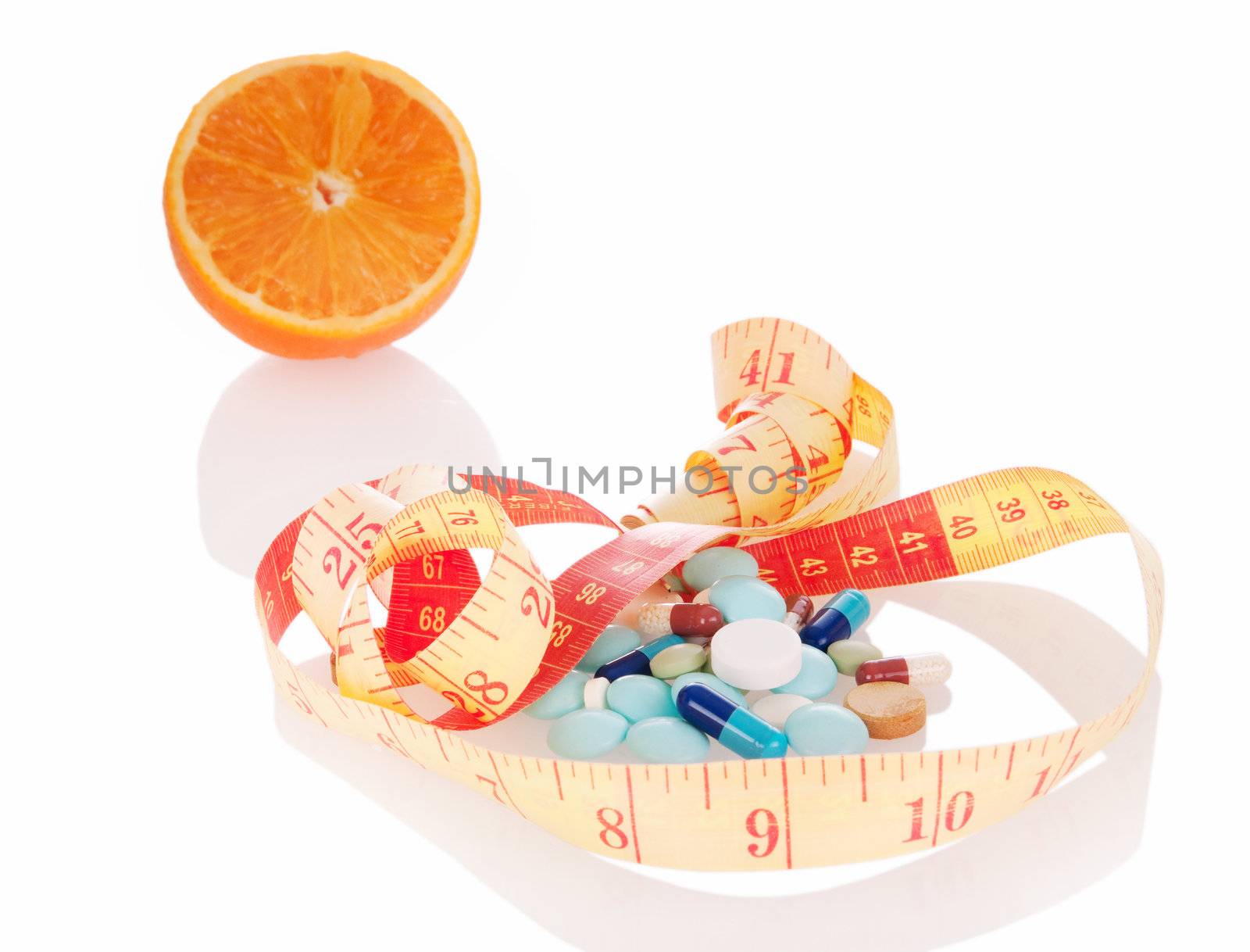 Concept of diet and medicine.  Heap of pills, orange slice and measuring tape with reflection on white background. Focus on pills