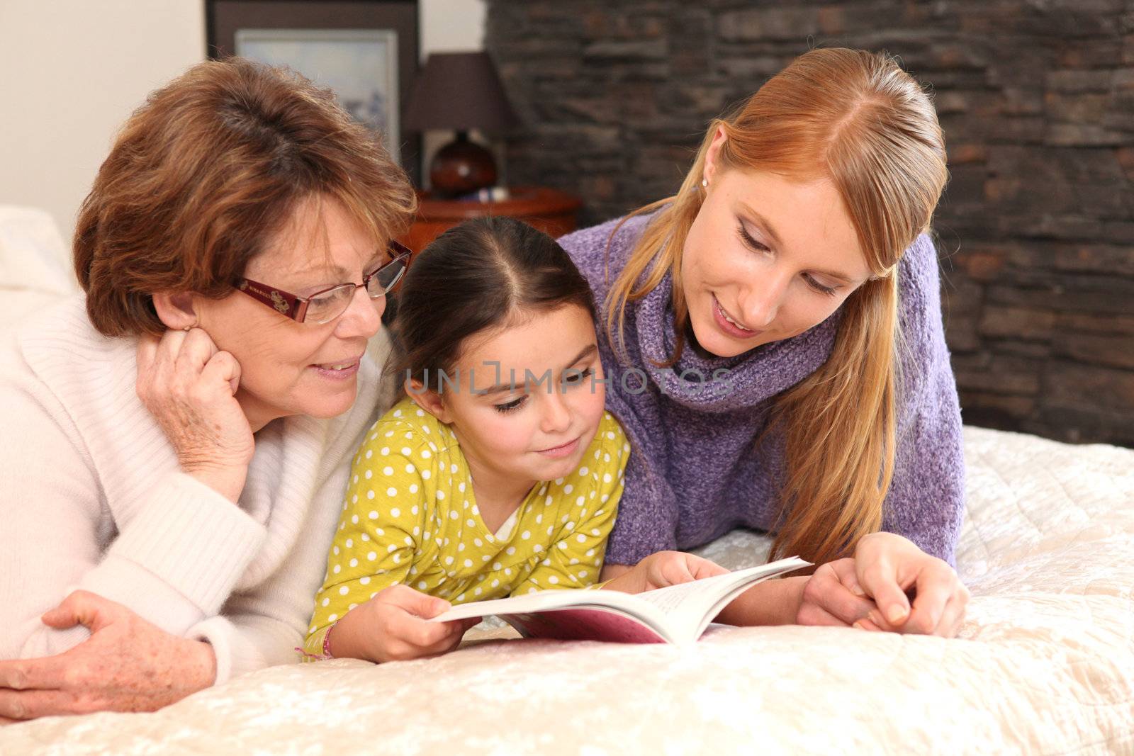 Three generations reading a book together by phovoir