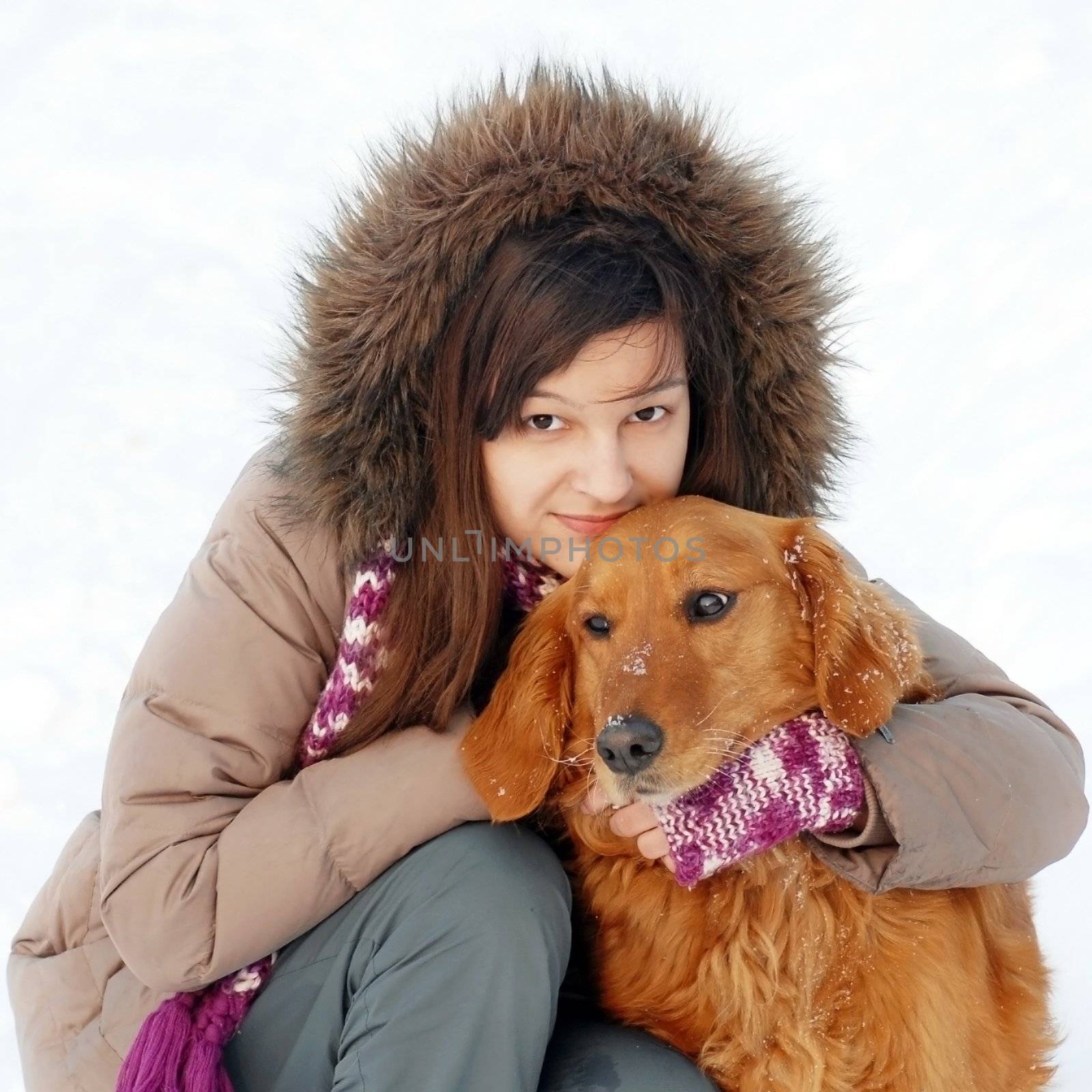 smiling teenager caucasian girl in hood hugging her dog outdoors at snow