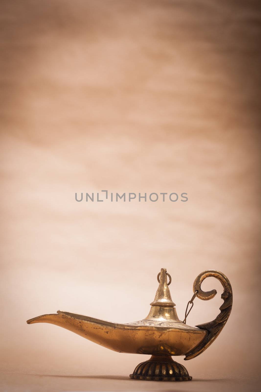 A magic genie lamp, isolated on a sand color background, in a studio shot.