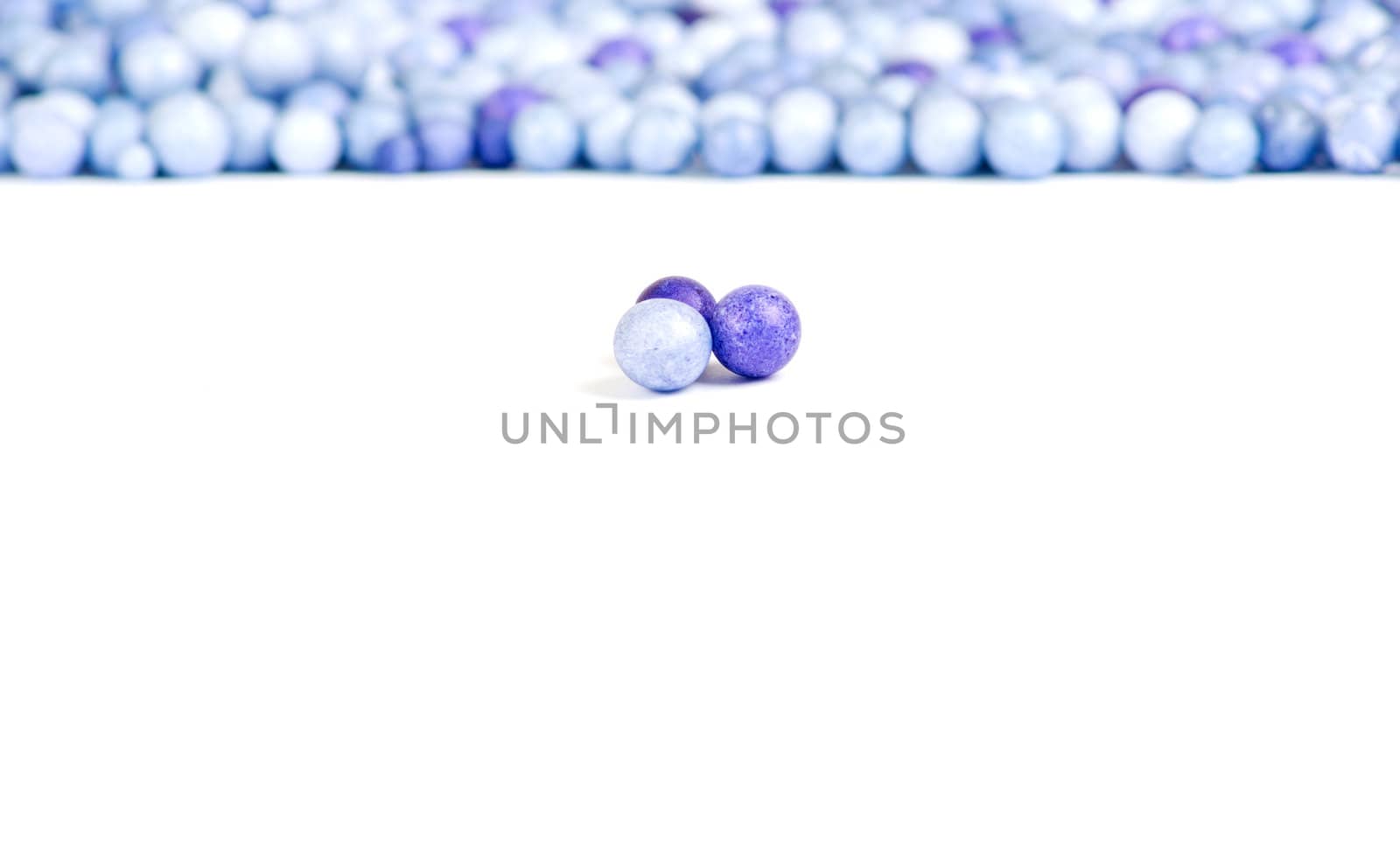 One blue and two violet little pearls isolated on background of other pearls.