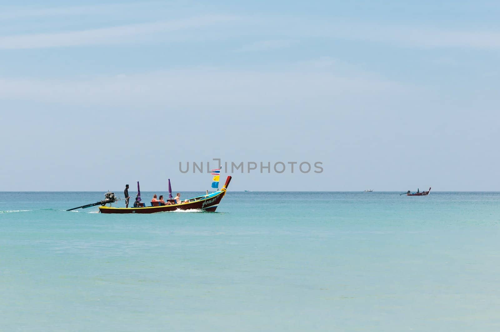 Karon, Phuket, Thailand - January 08, 2012: Traditional wooden Thai tourist boat with tourists on calm blue sea near Karon beach