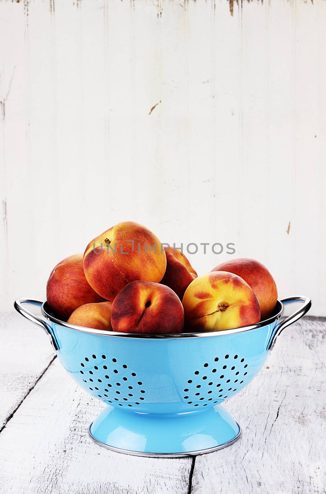 Blue colander filled with fresh peaches over a rustic background.
