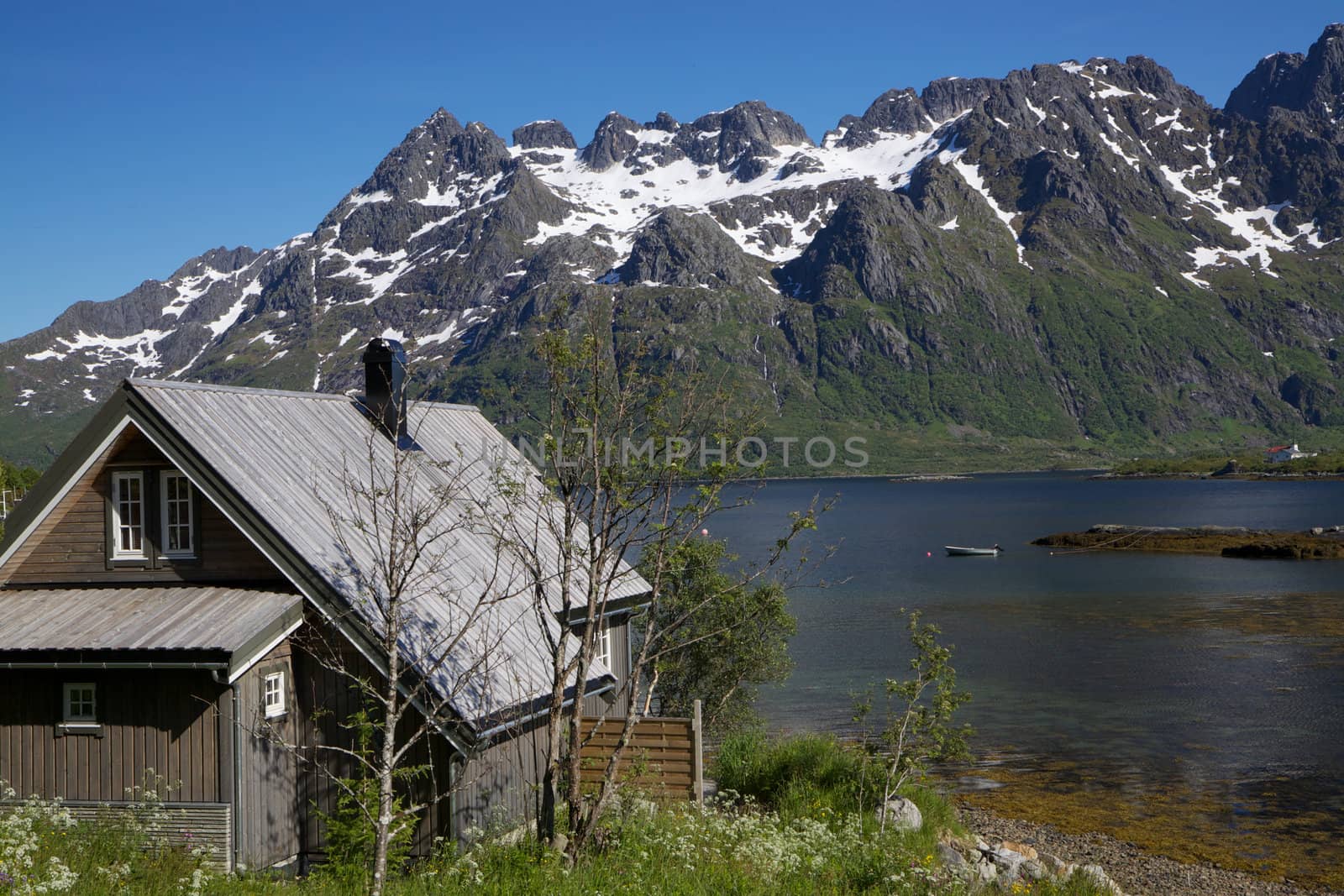 Wooden hut by the fjord surrounded by snowy peaks of mountains on Lofoten islands in Norway