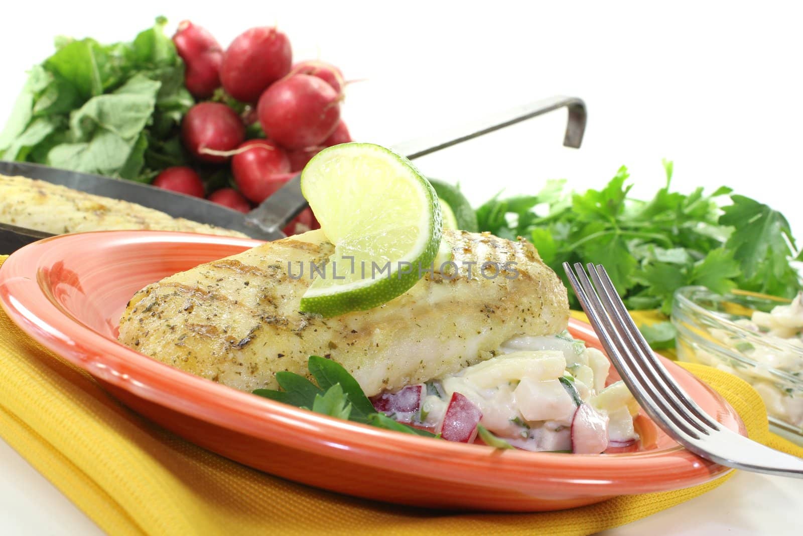 Hake with potato salad and slice of lime on a light background