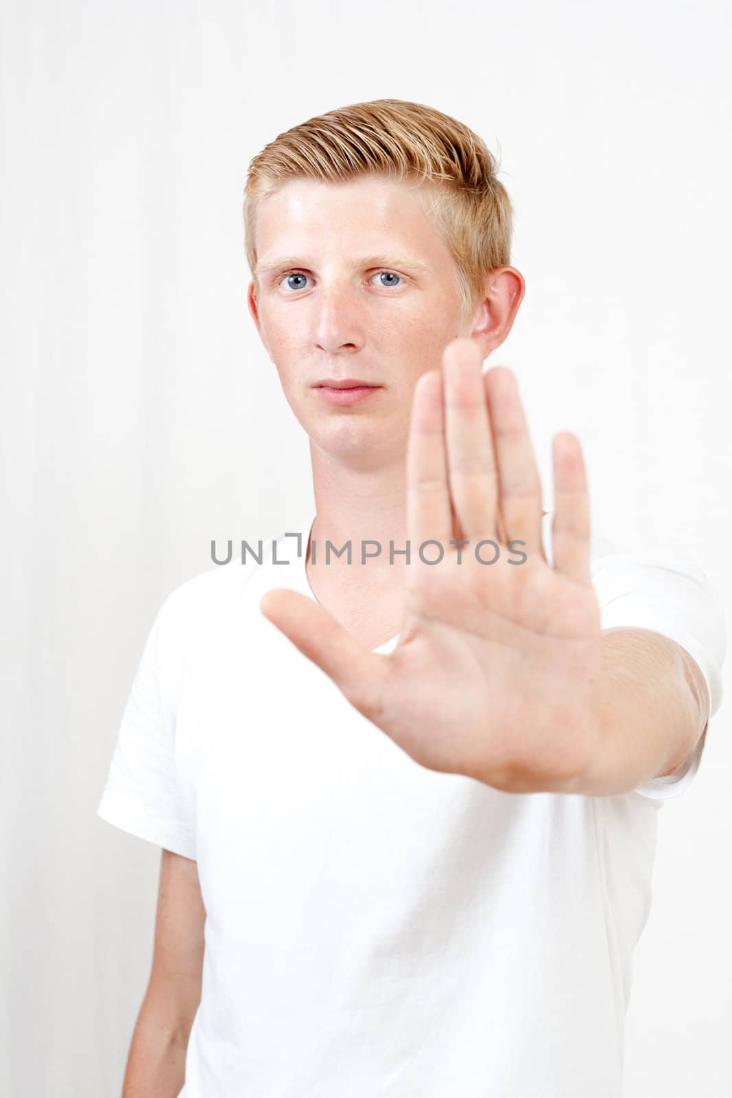 young man with blue eyes makes stop gesture/holds up hand