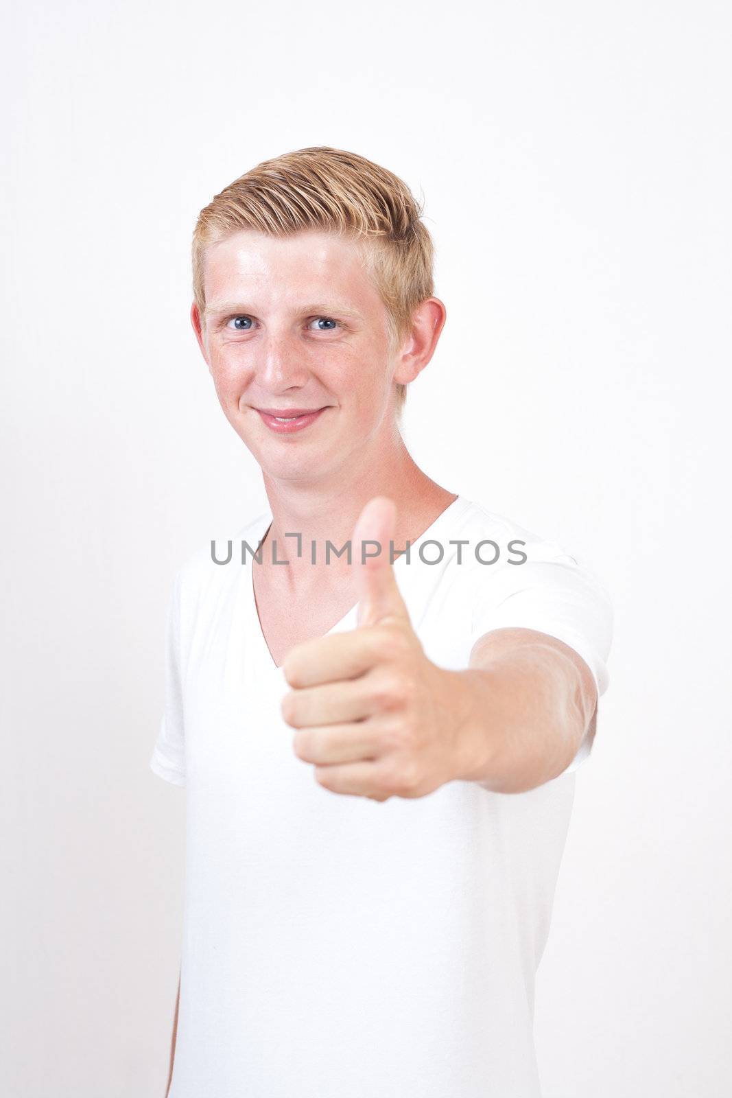 young man with blue eyes gives the thumbs up gesture on grey background