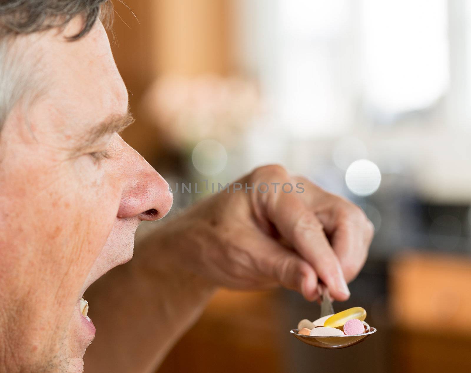 Senior caucasian male eating a spoonful of vitamin tablets for breakfast in kitchen