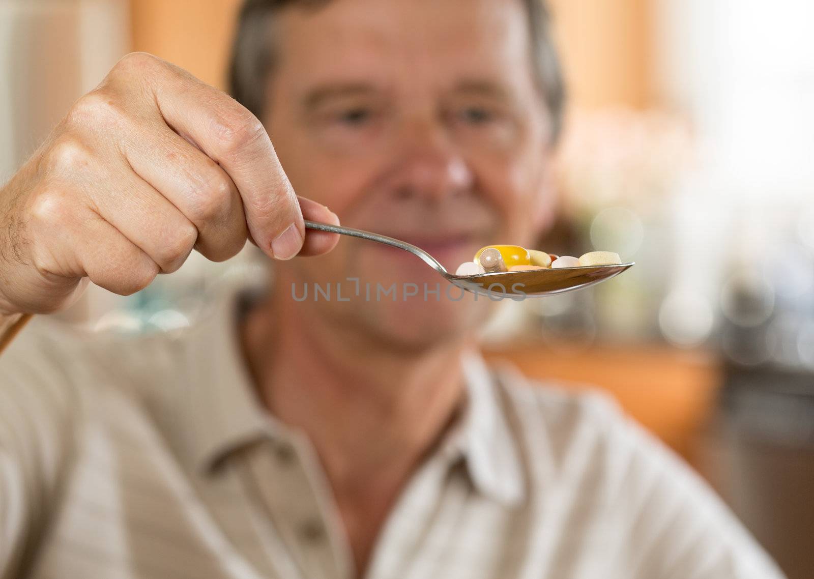 Senior caucasian male eating a spoonful of vitamin tablets for breakfast in kitchen