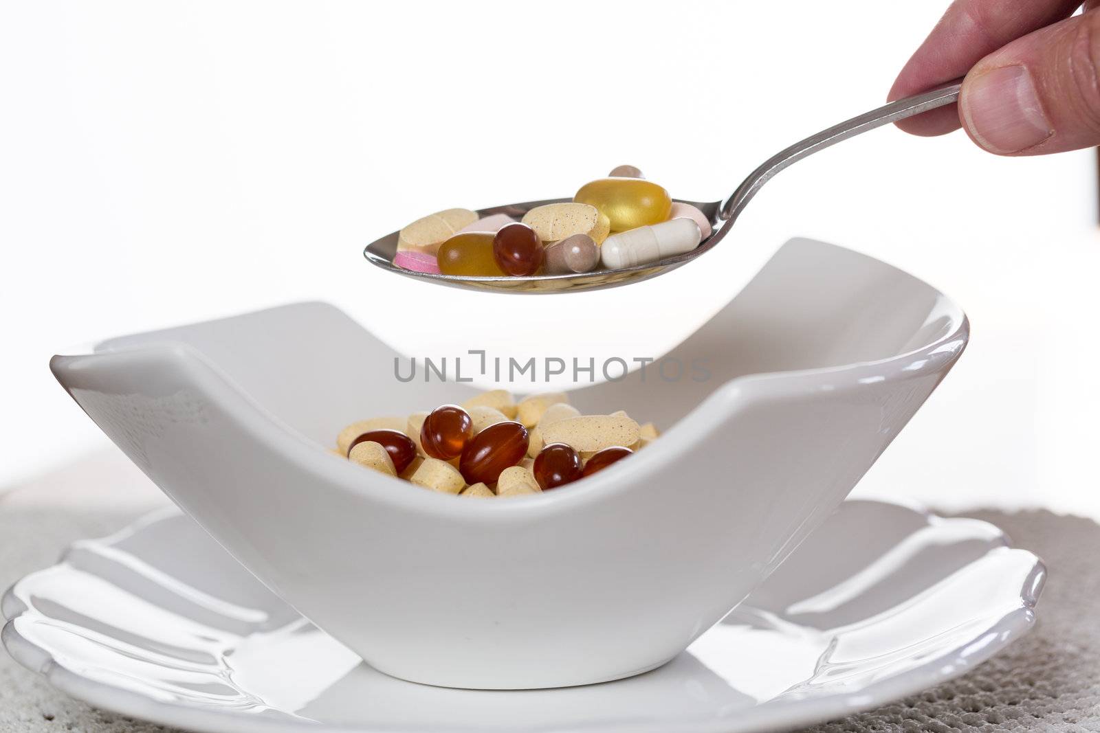 Spoonful of vitamin tablets suspended over bowl of tablets for breakfast in kitchen