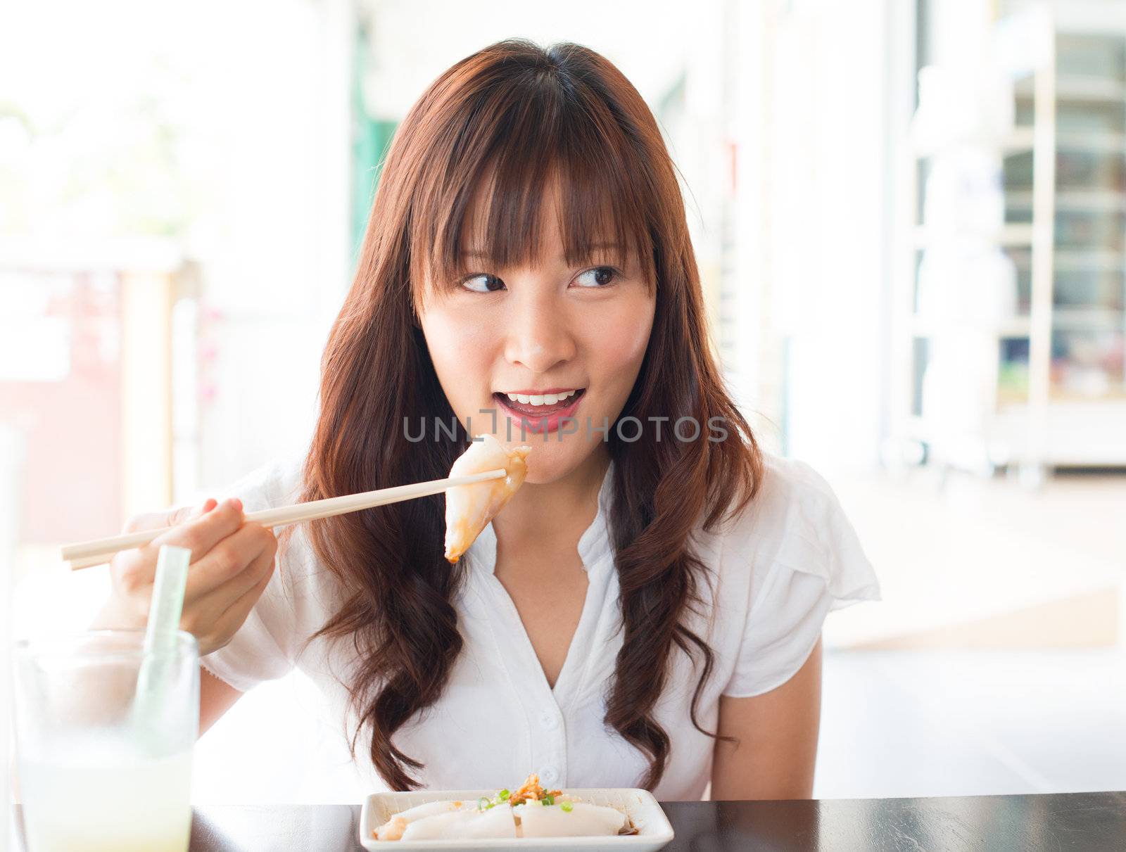 Eating rice noodle roll (chee cheong fun) at restaurant. Young Asian girl eating breakfast Cantonese cuisine dim sum using chopsticks.