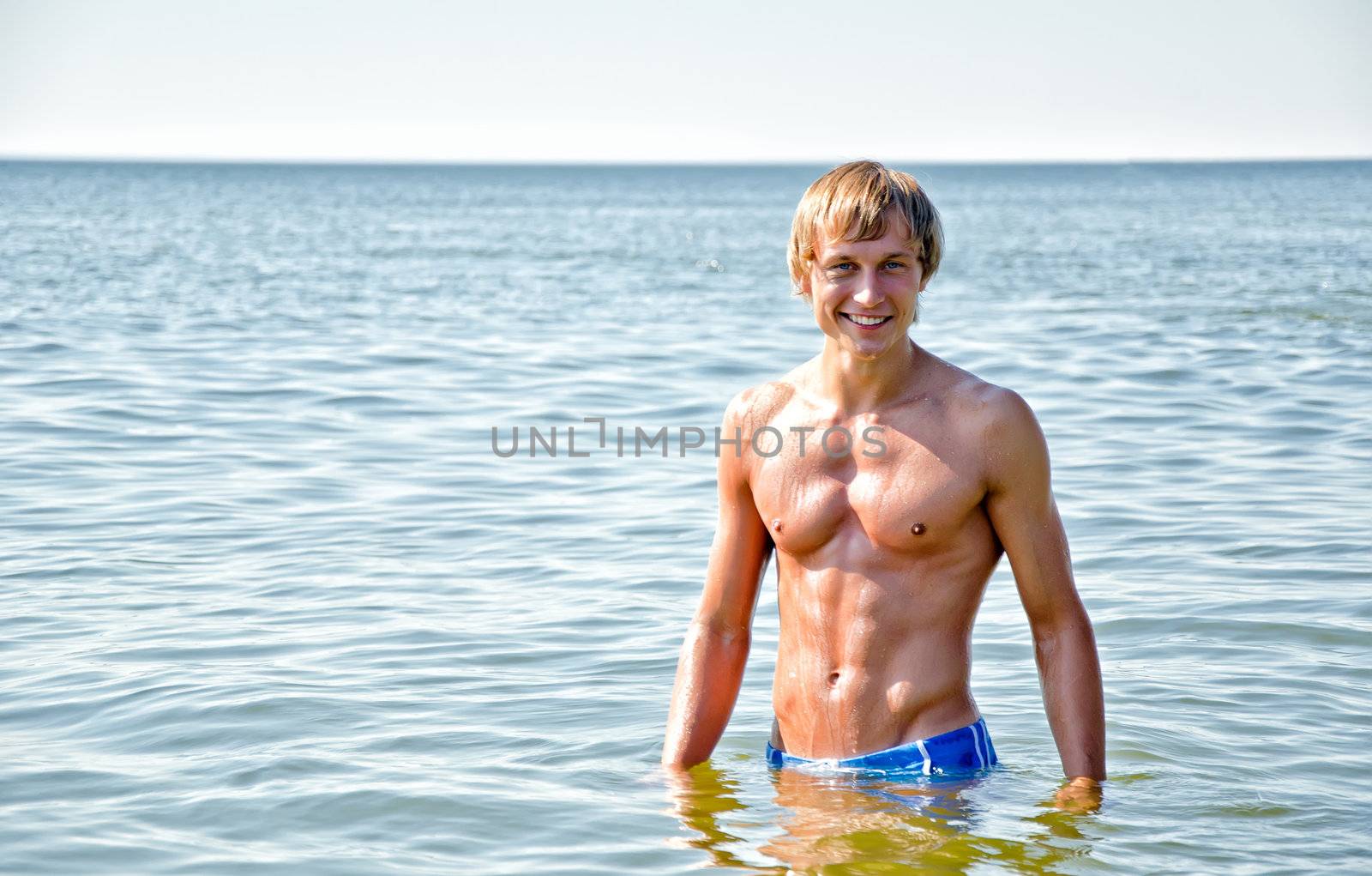 Semi nude handsome smiling man standing in the sea