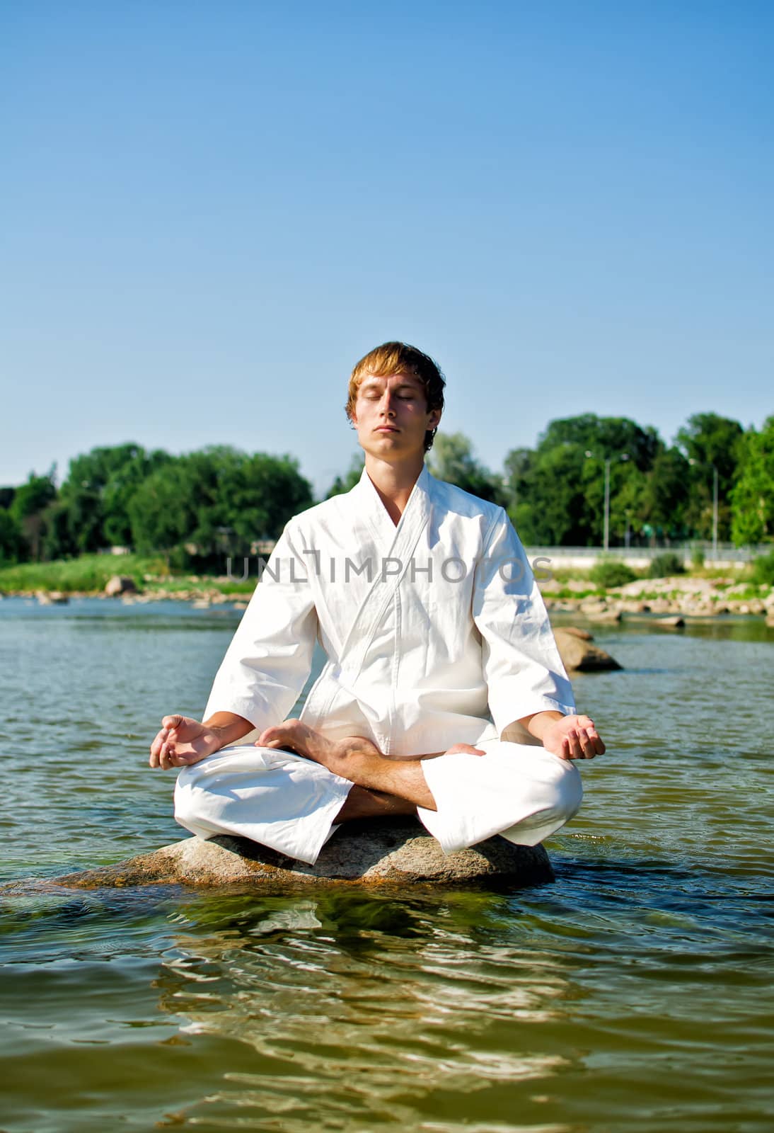 Man in kimono meditating on the rock in the sea