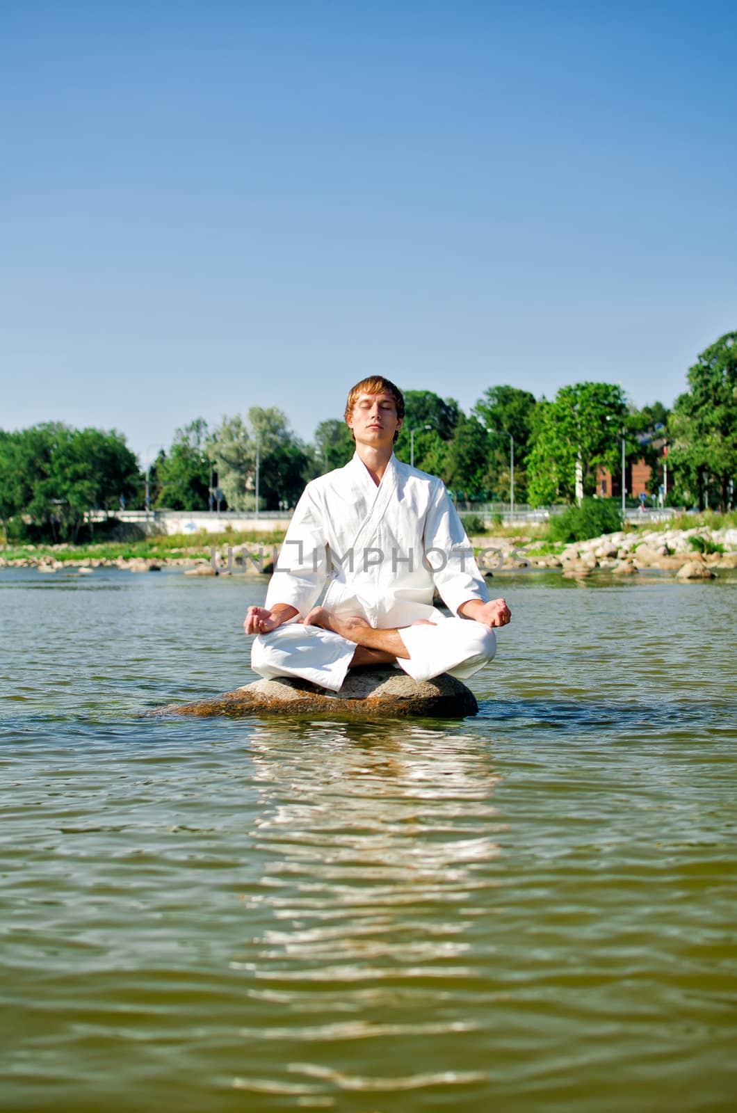 Man in kimono meditating on the rock in the sea