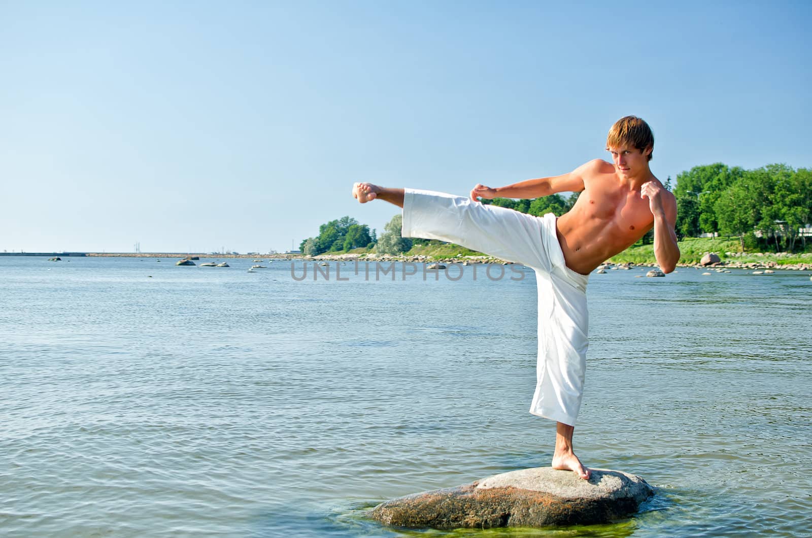 Man in kimono training on the rock in the sea