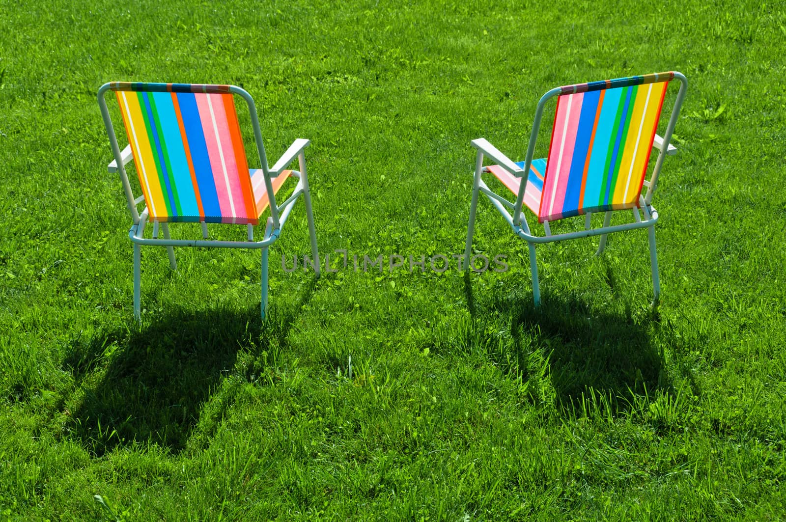 Two colorful chairs standing on grass at back yard