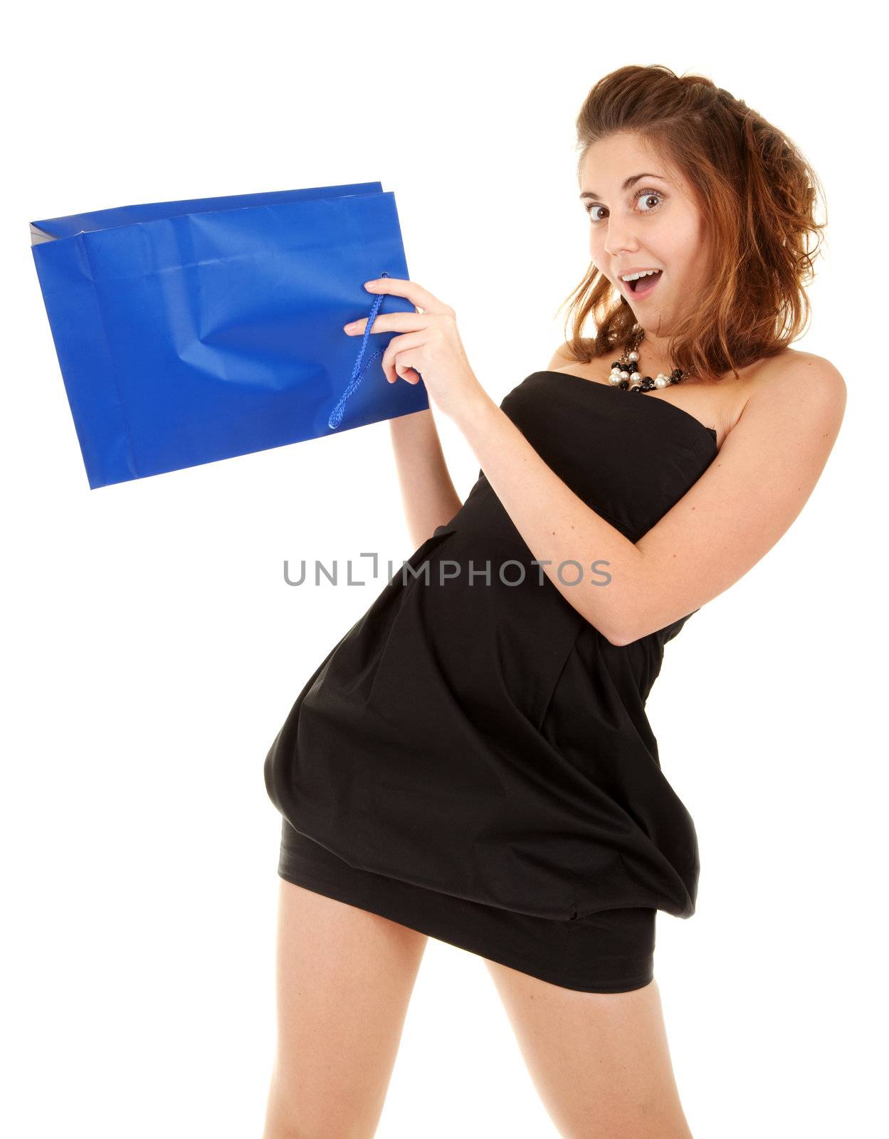 Surprised beautiful women in short black dress with blue paper bag try to discover what is inside the bag.