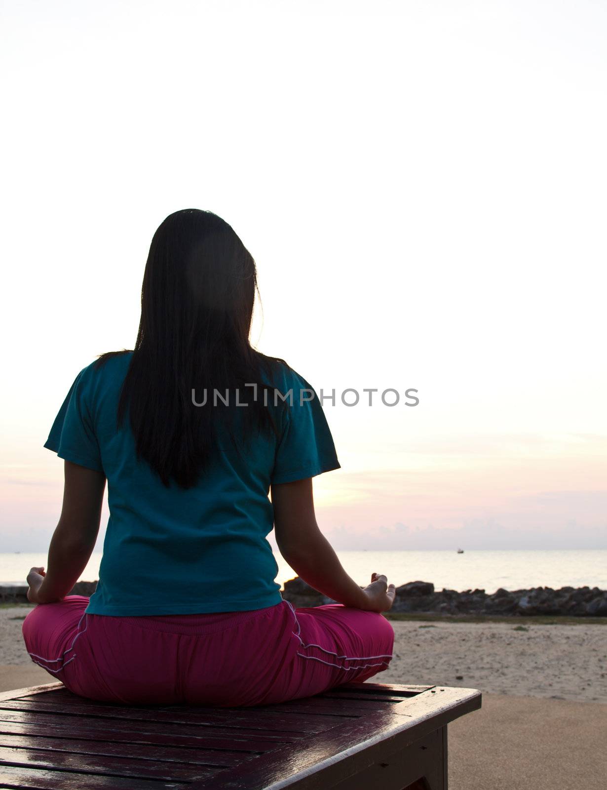 Woman meditating on the beach at sunset.  by tiverylucky
