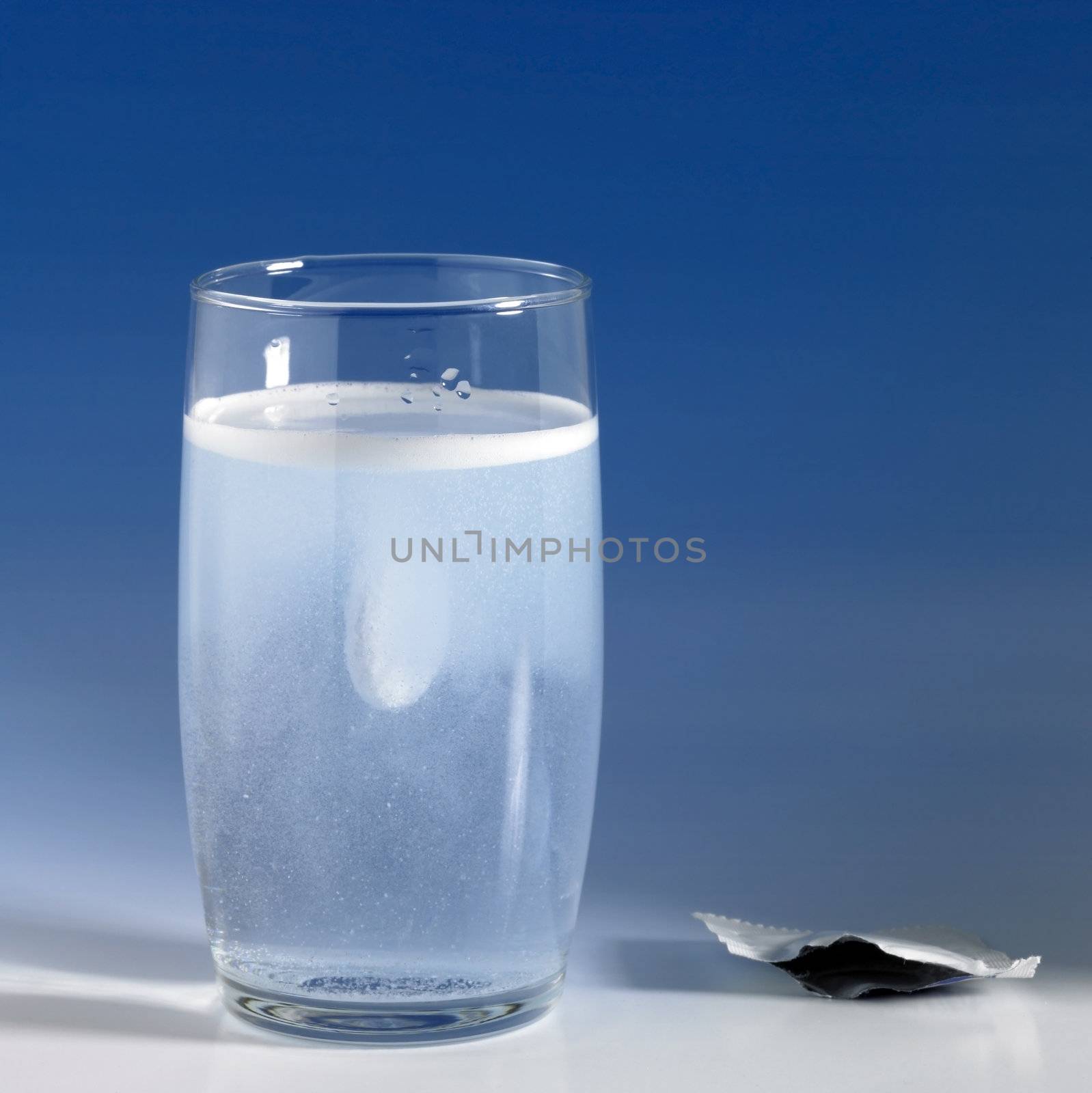dissolving fizzy tablet in a glass of water. Studio photography in blue gradient back