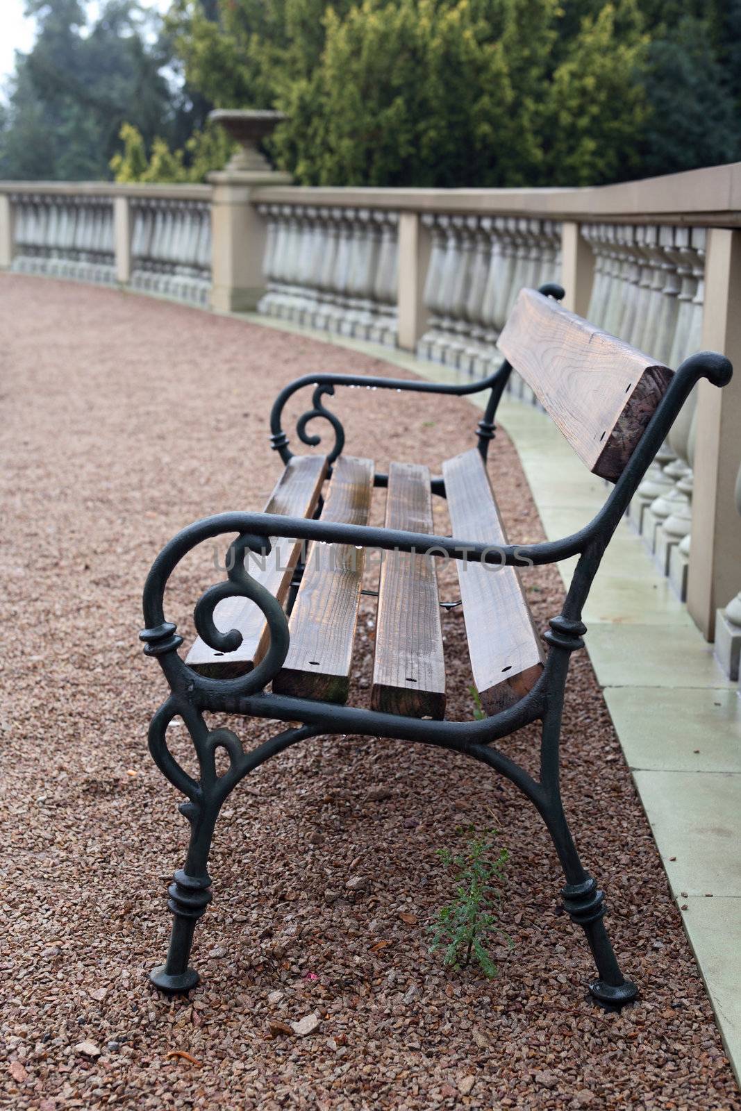 Stylish wooden park bench near stone fence after rain