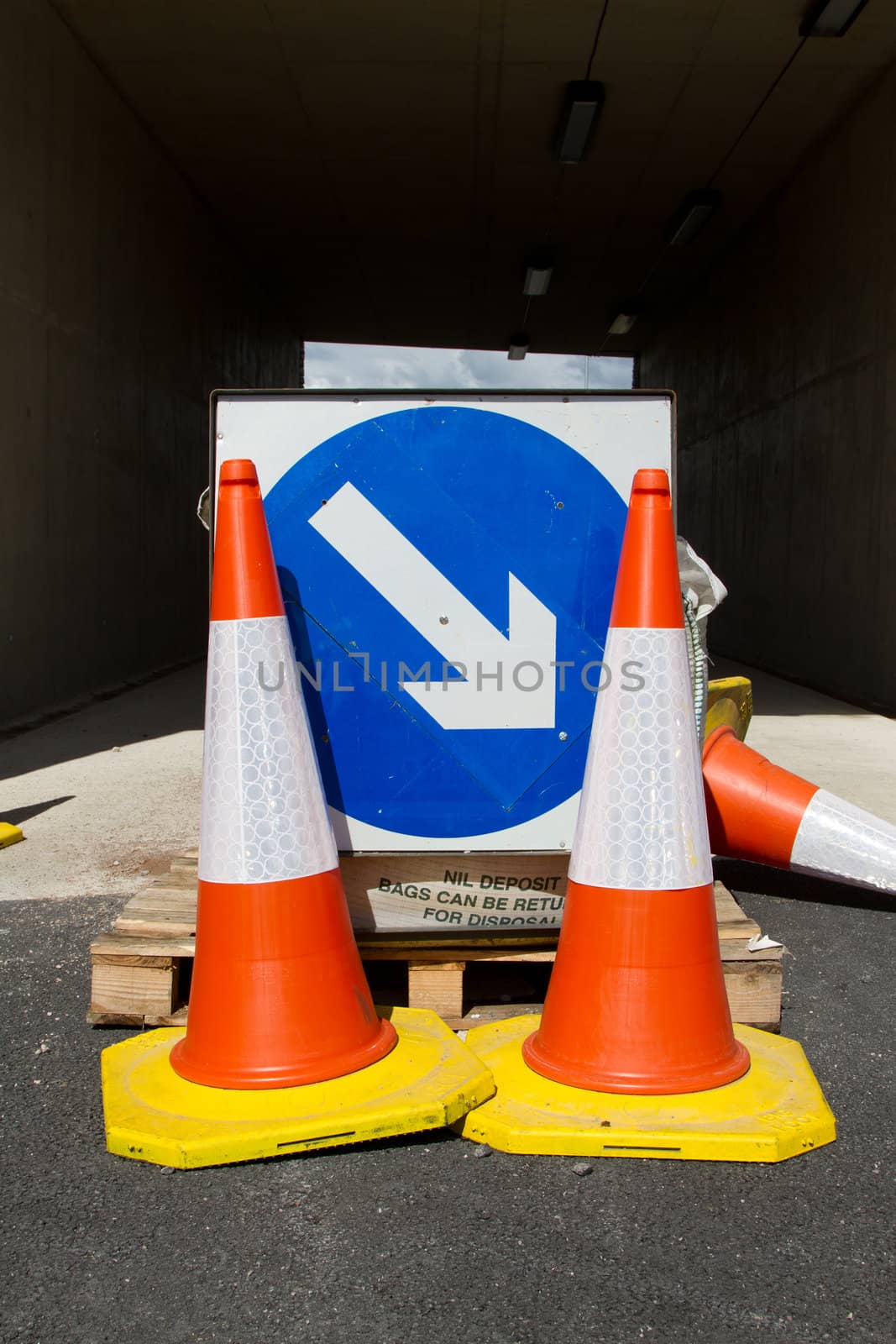 A pair of red, white and yellow bollards in front of a blue circular sign with a white arrow.