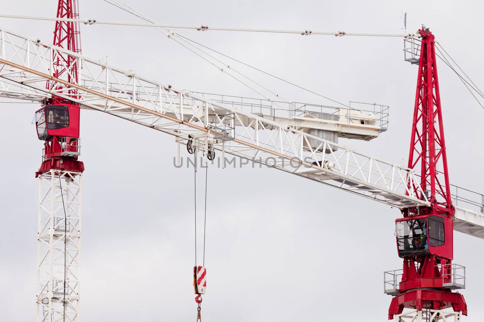 Detail of two large steel construction cranes with red operator cabs for hoisting heavy loads during building construction and development