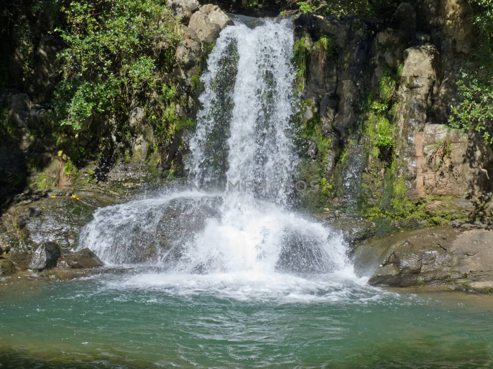 Natural waterfall casdcading over rocks into a calm blue pond below