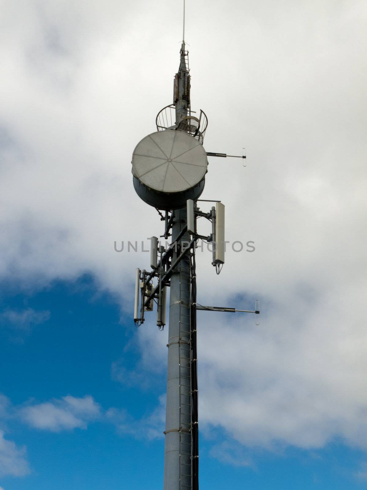 Metal tower with mobile cell phone telecommunications antennas against cloudy blue sky with copyspace