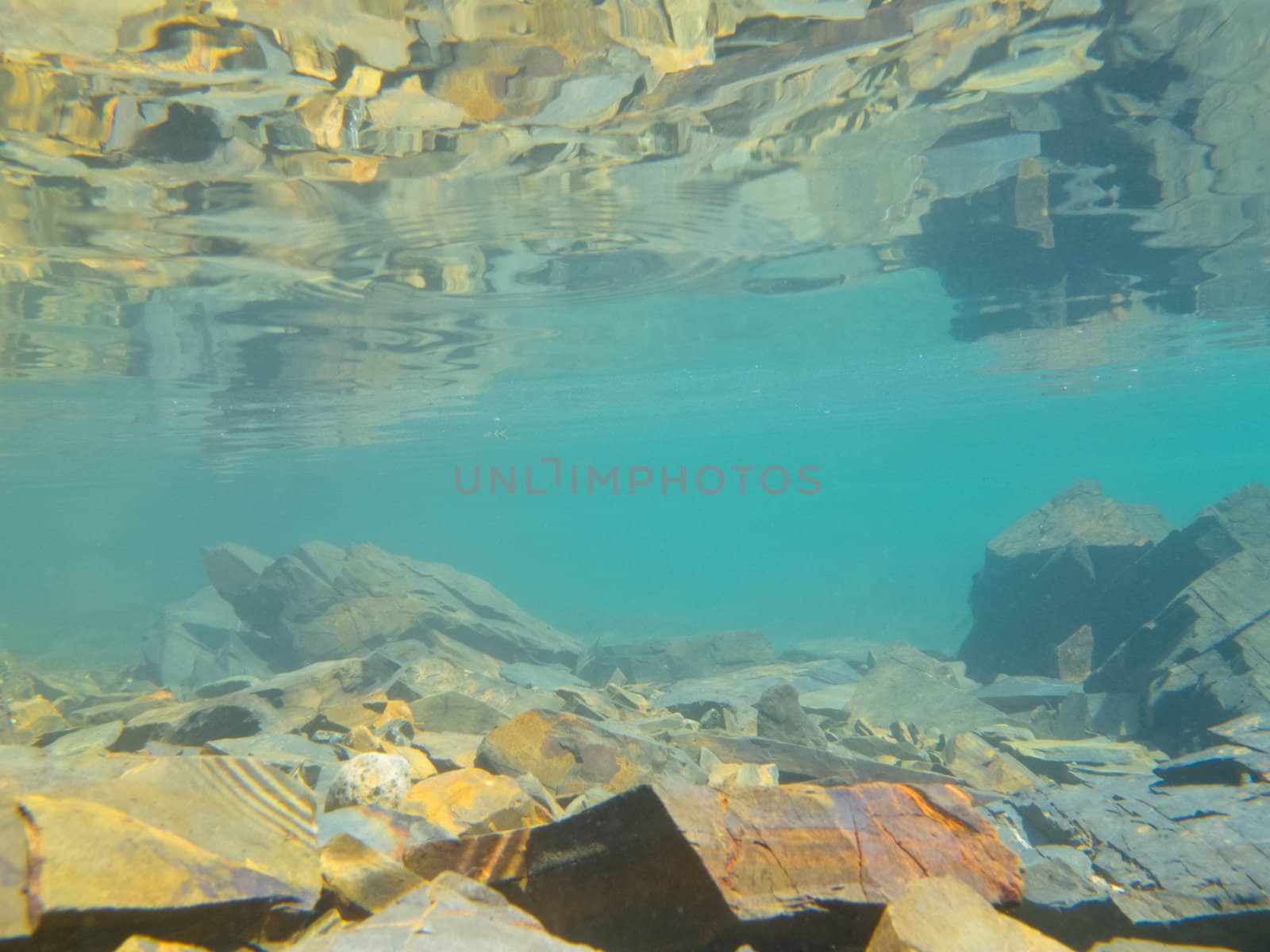 Underwater shot in shallow water over submerged rocks with reflection of rocky bottom from underneath calm surface