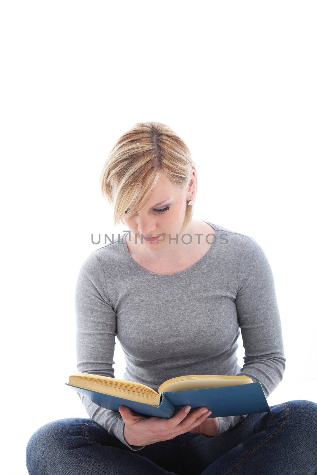 Young female student sitting cross legged on the floor stydying from a textbook isolated on white 