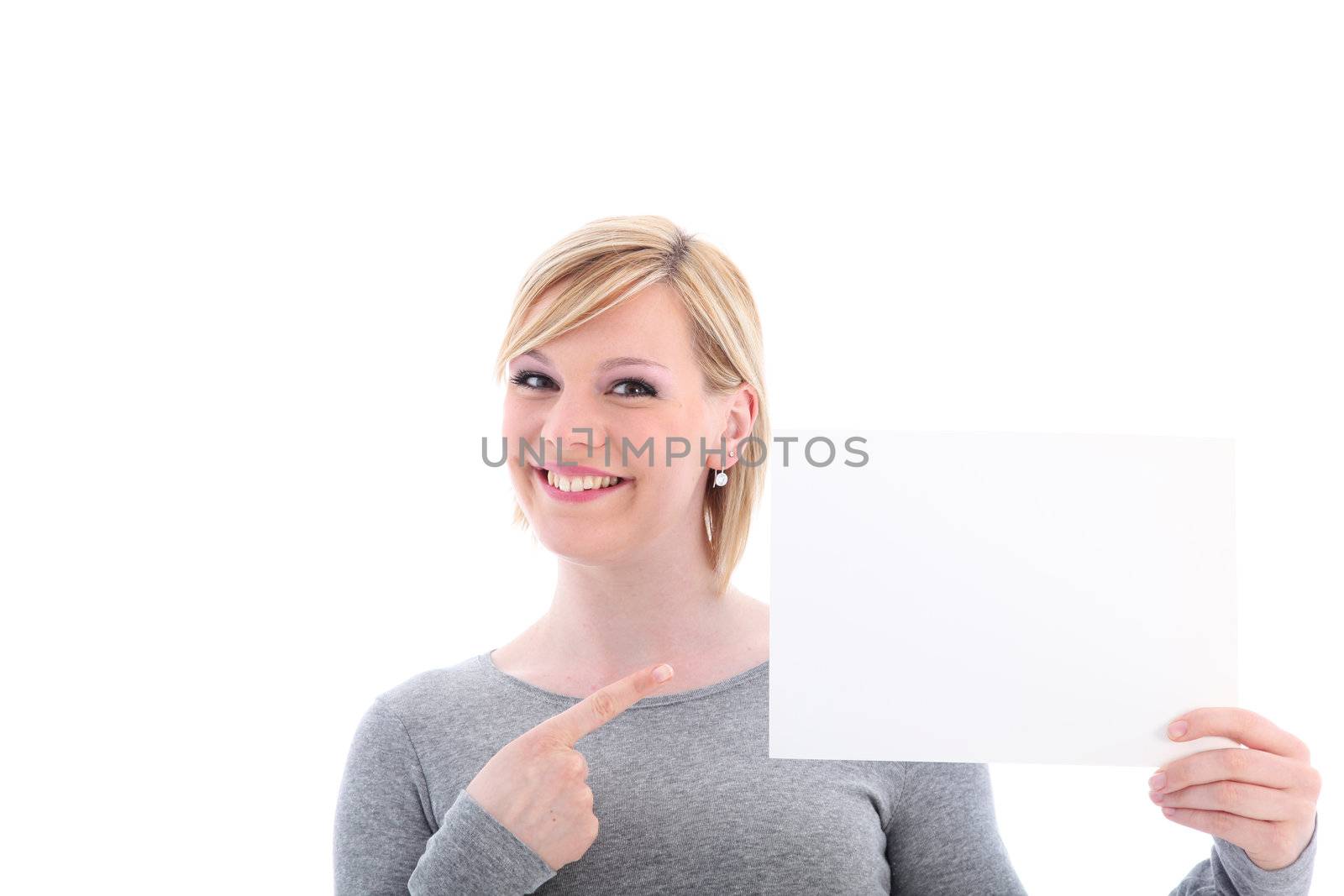 Smiling woman pointing with her finger to a blank sign that she is holding up to the side of her face isolated on white 