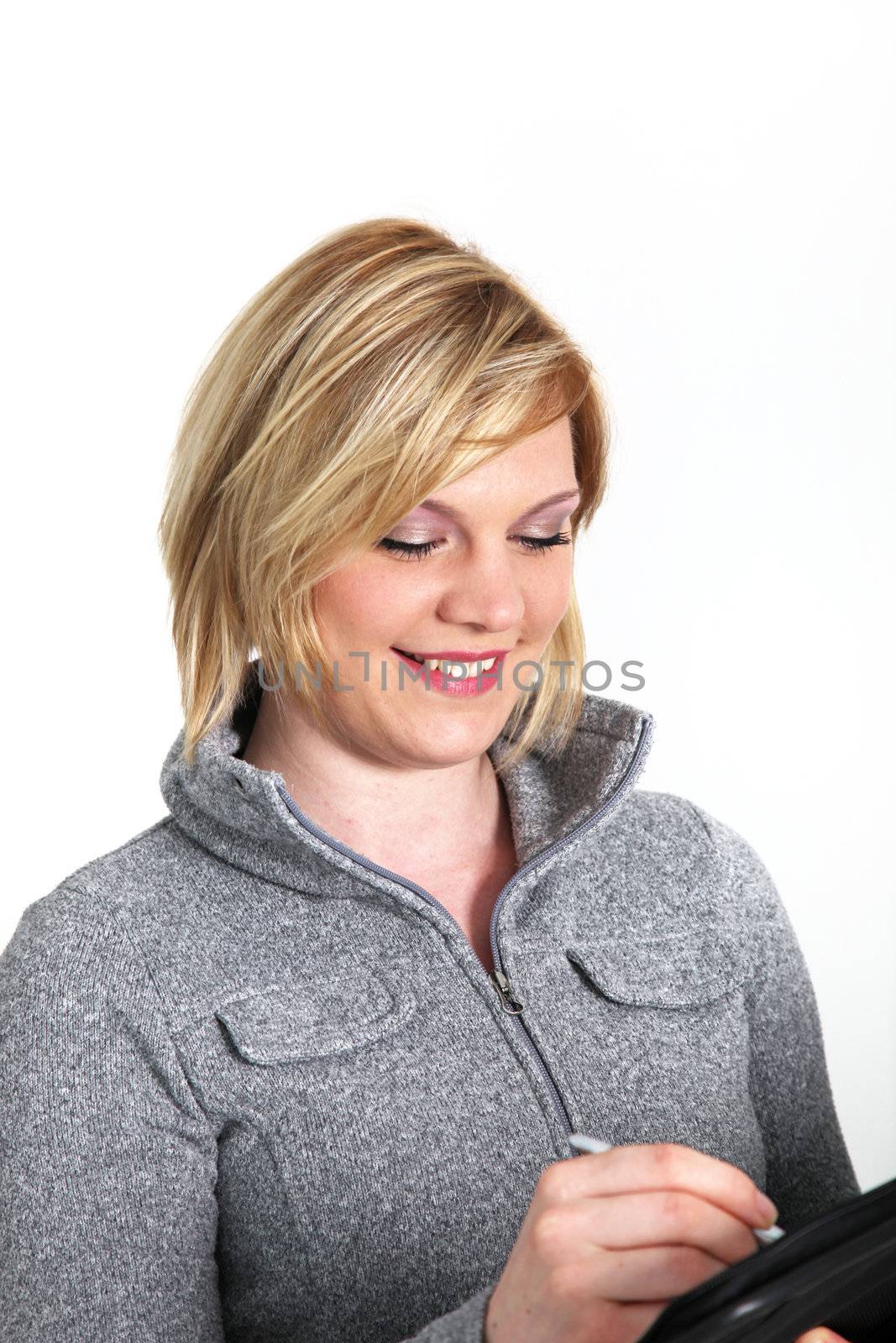 Pretty smiling young blonde woman in a grey winter top writing notes in a handheld file 