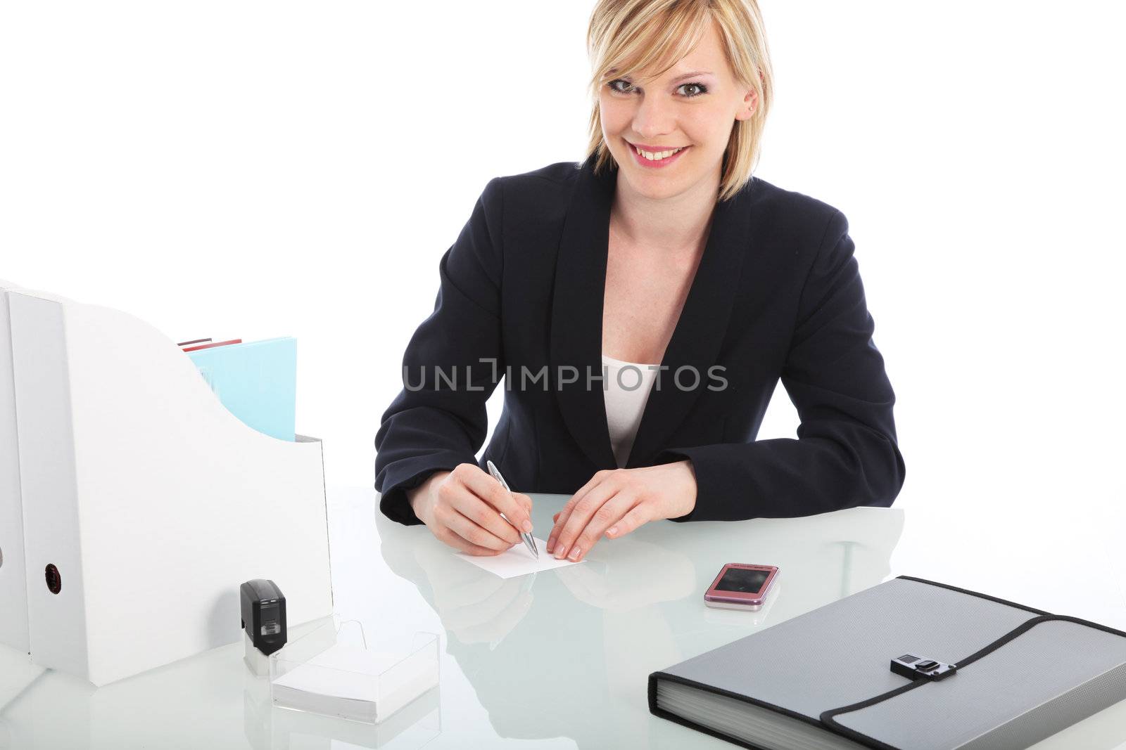 Smiling businesswoman seated at a desk writing out a memo in a white office 