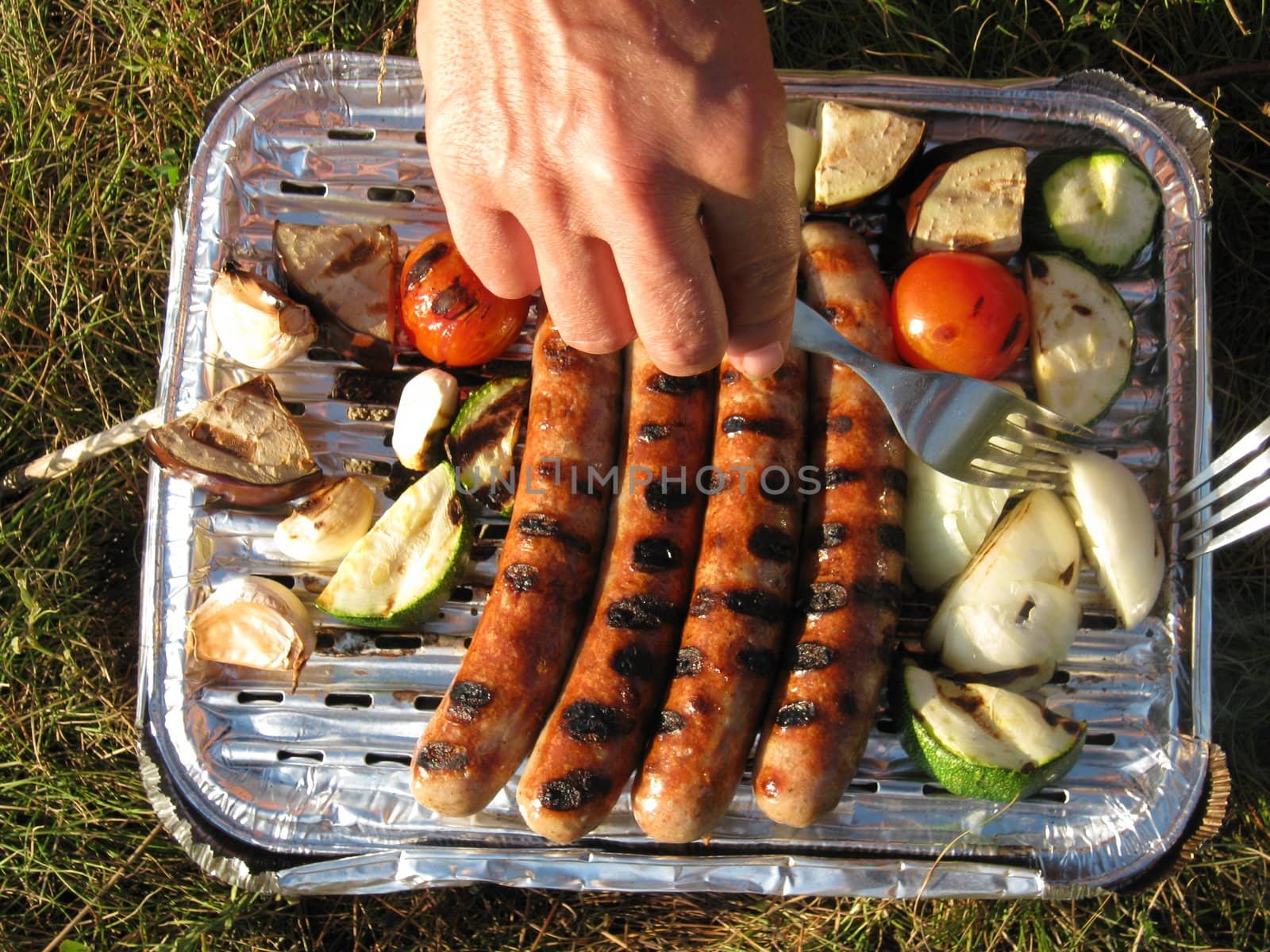 Hands on a disposable barbecue with sausages and vegetables          