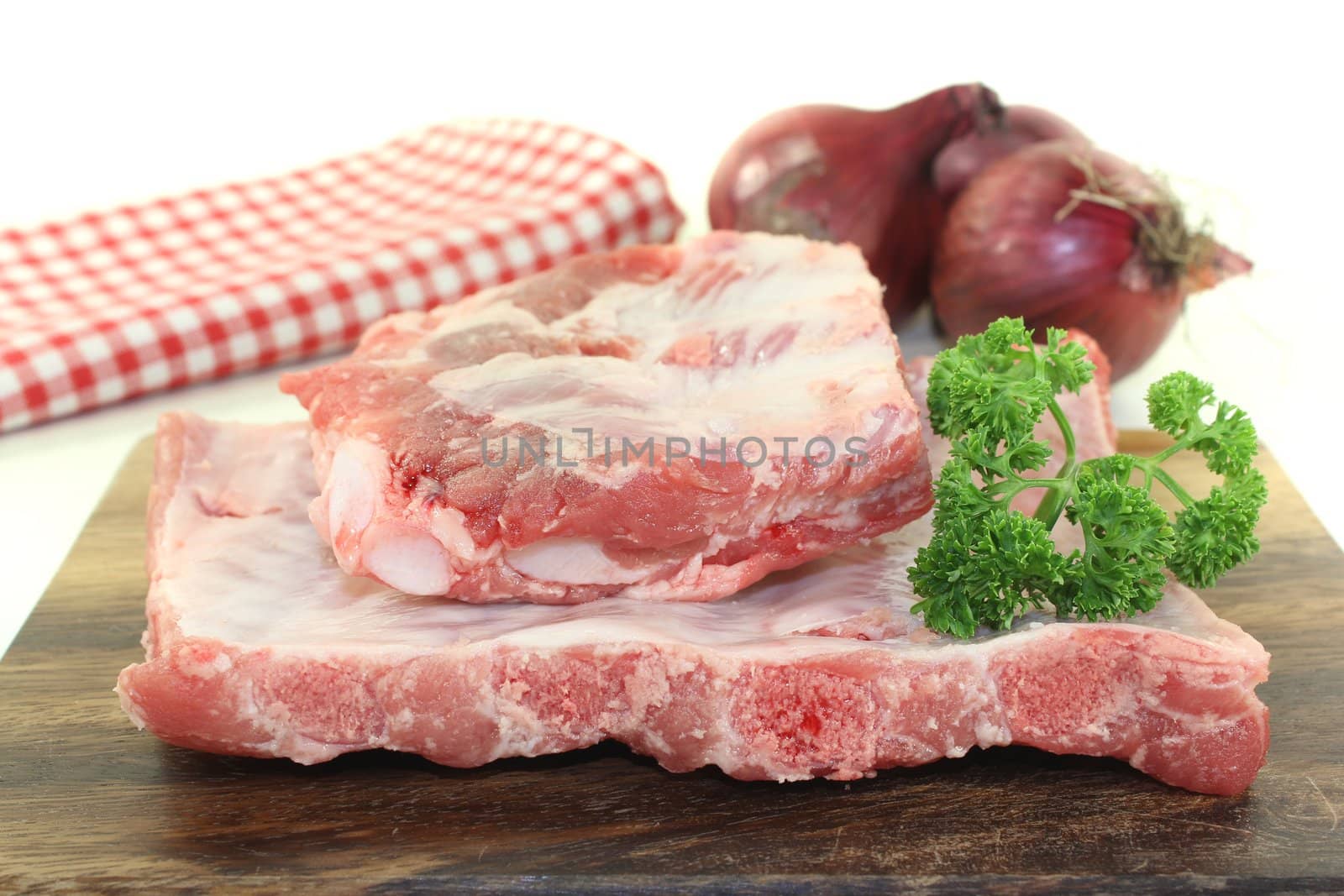 Beef spare ribs with parsley and onions on a wooden board in front of light background