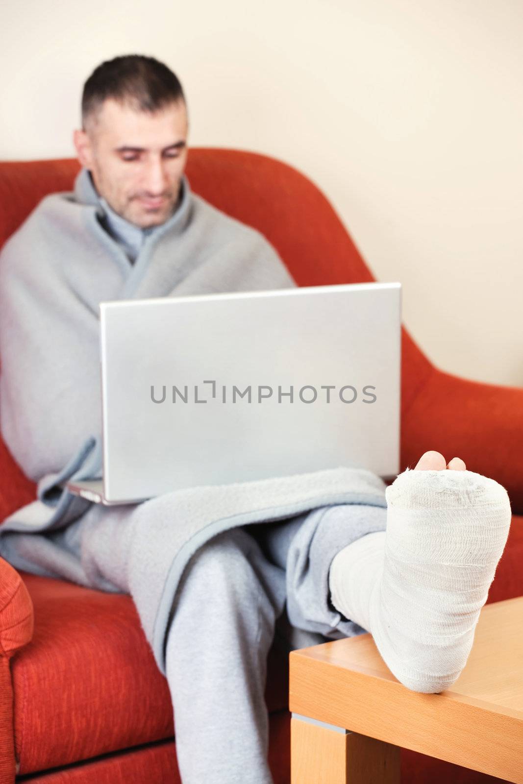 man with a broken leg on a sofa at home  working on laptop