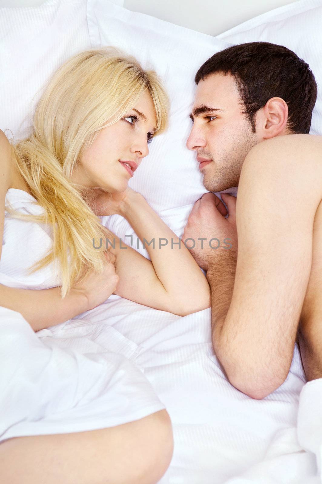 Young couple in bed having conversation on pillow