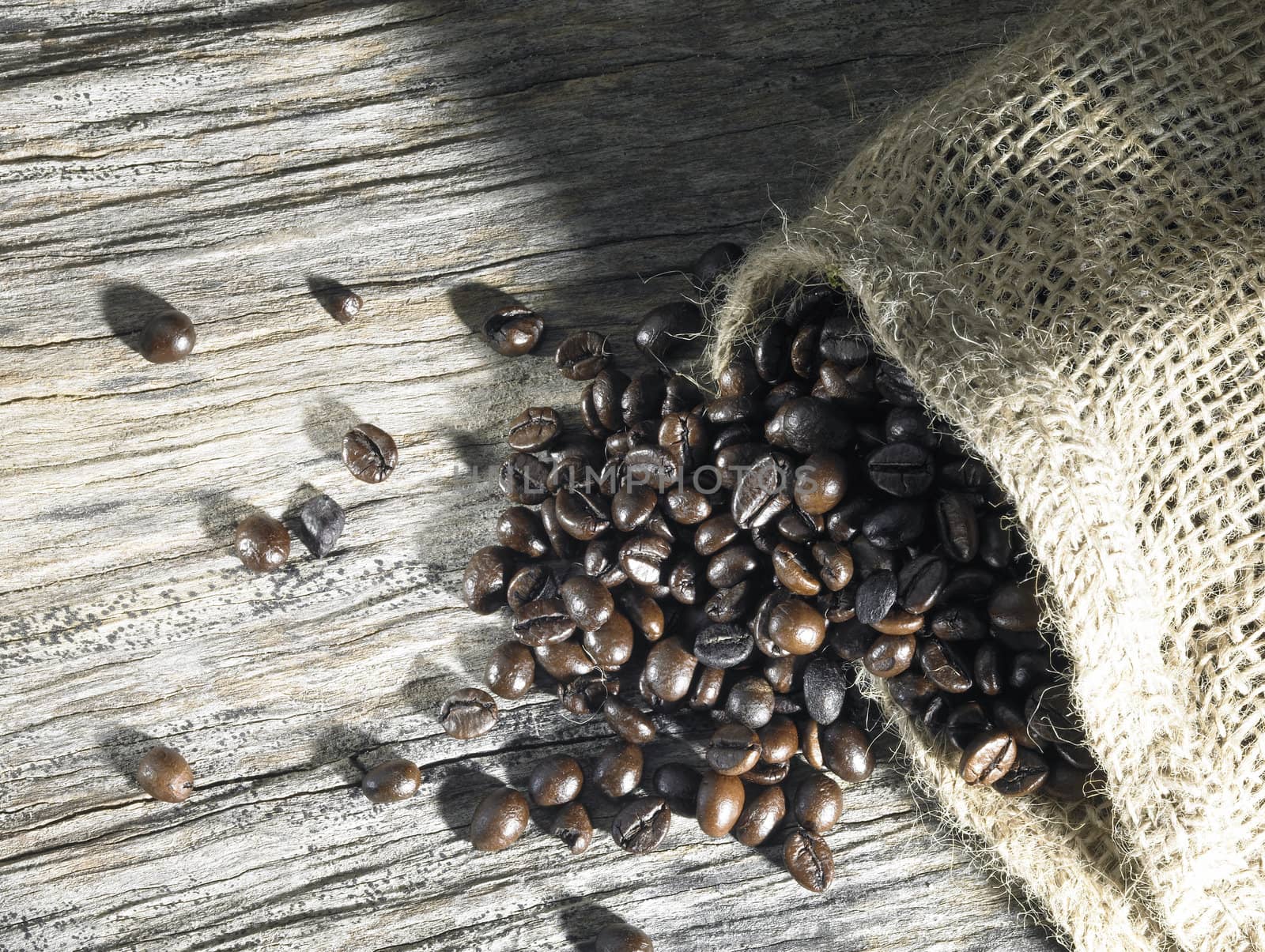 coffee beans fallen out of a jute bag located on weathered wood