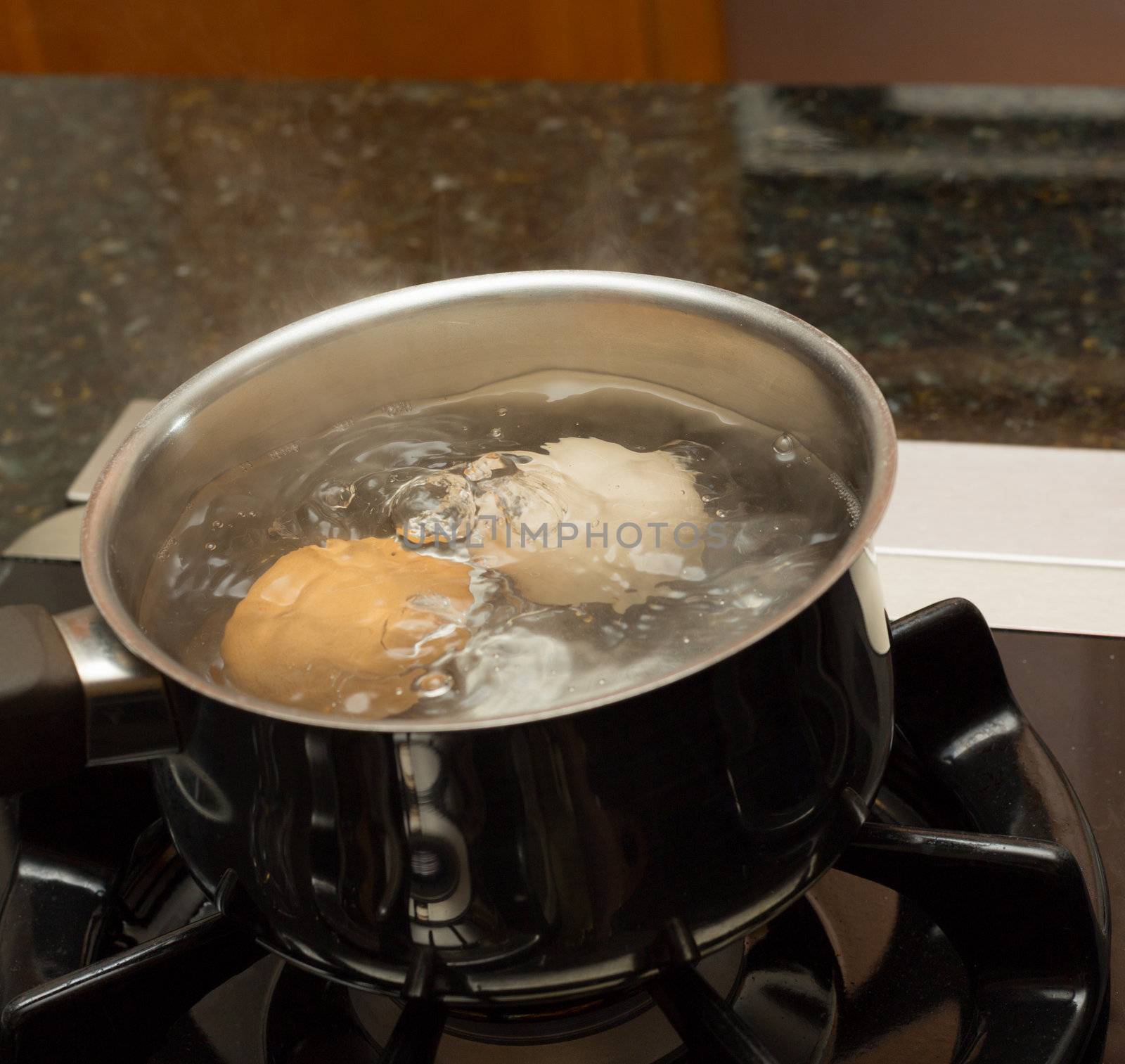 Two eggs in boiling water in stainless steel pan on gas hob