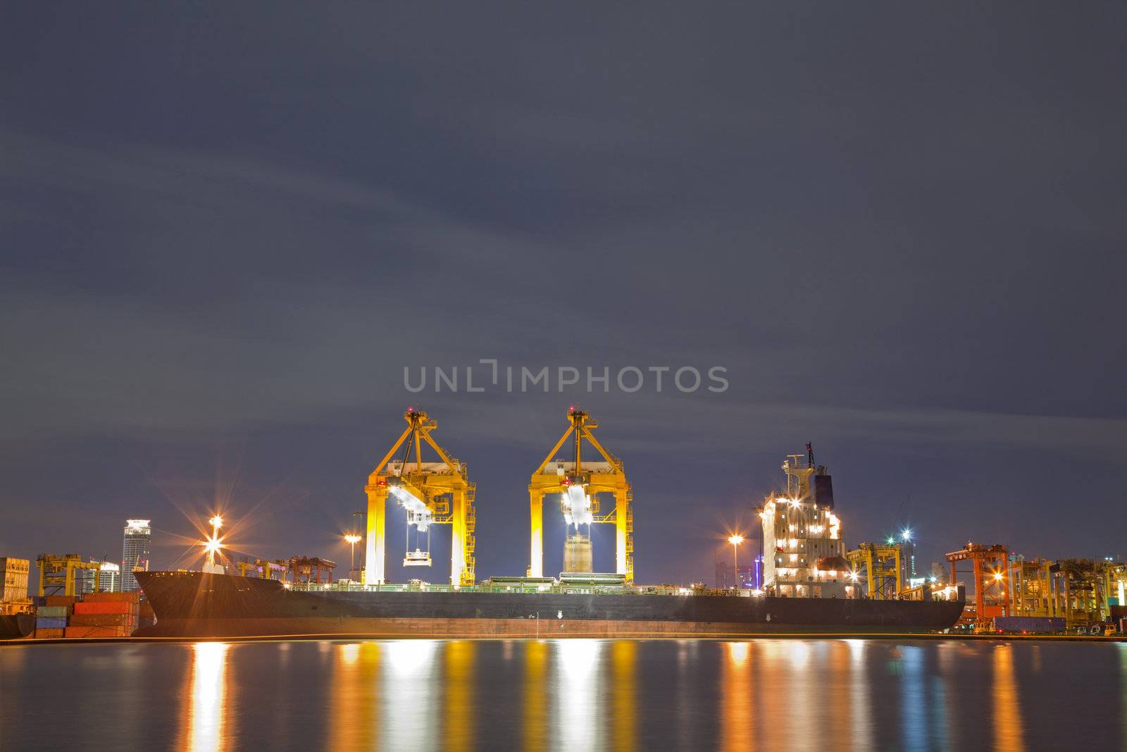 Industrial Container Cargo freight ship with working crane bridge in shipyard at dusk for Logistic Import Export background