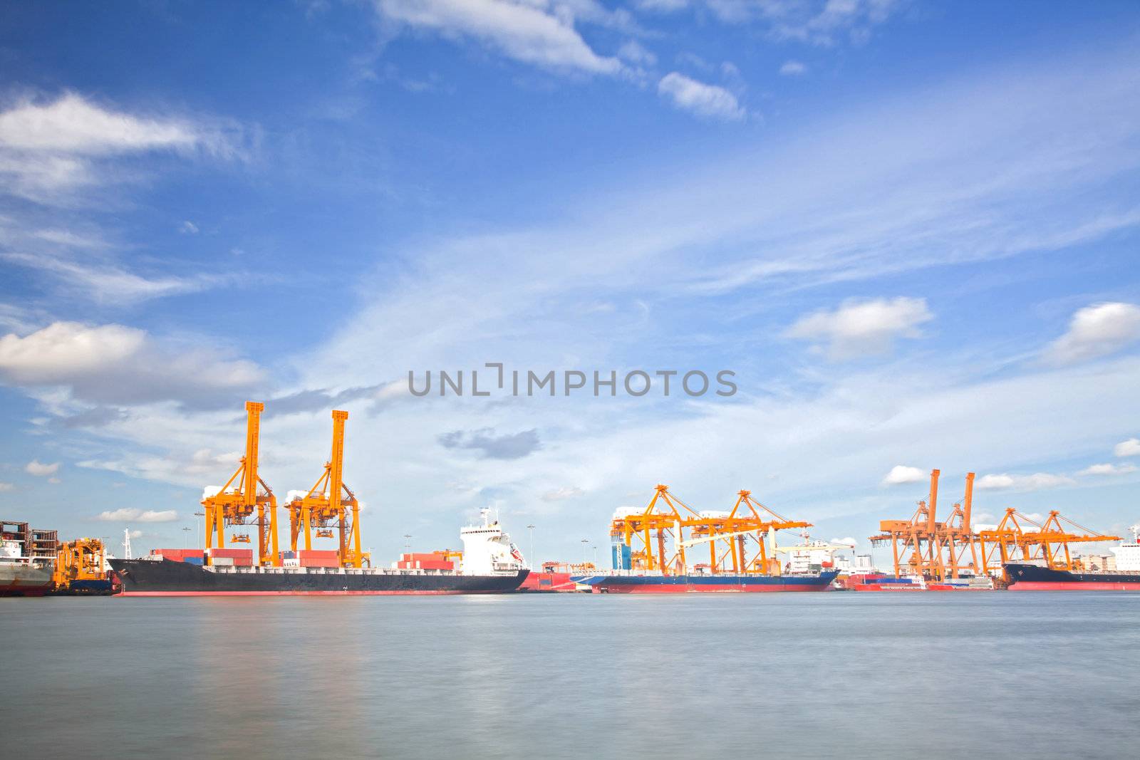 Cargo Ships Loading and unloading goods container with cranes at Port Terminal with beautiful cloudscape for heavy industry and logistic background