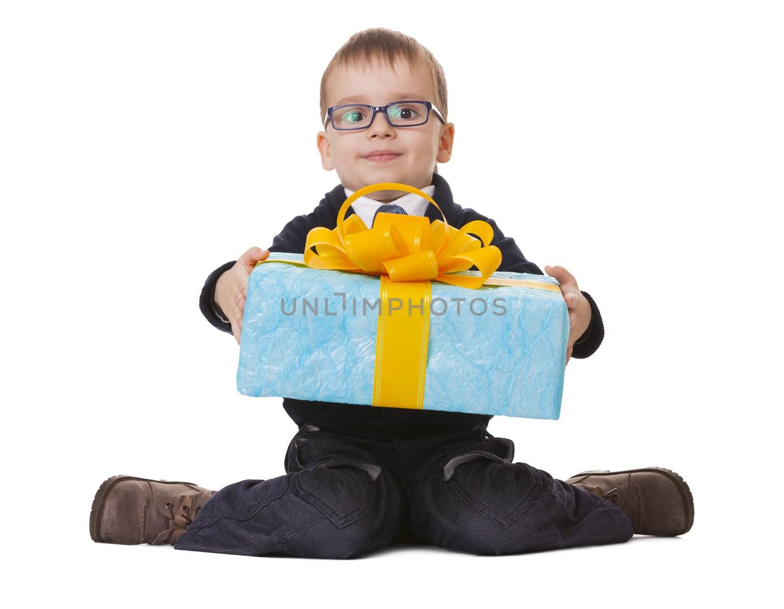 Small sitting boy in spectacles holds a big blue present on white background