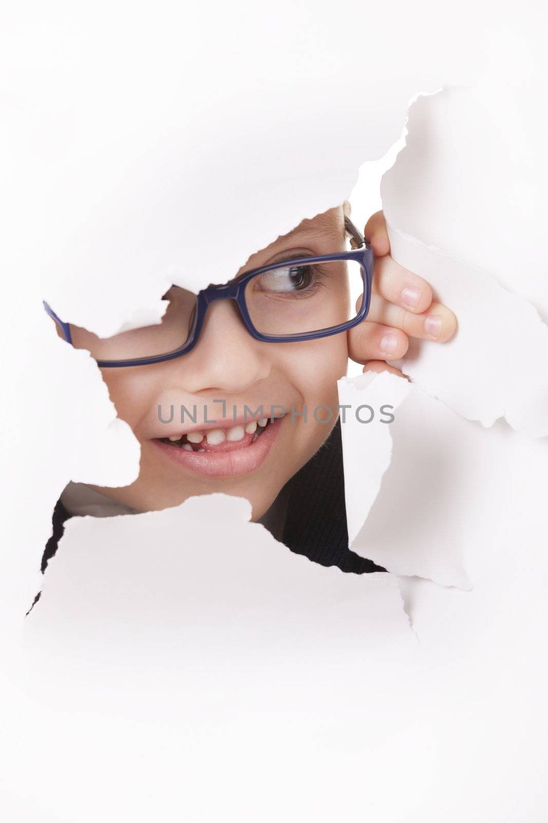 Curious kid in spectacles looks through a hole in white paper