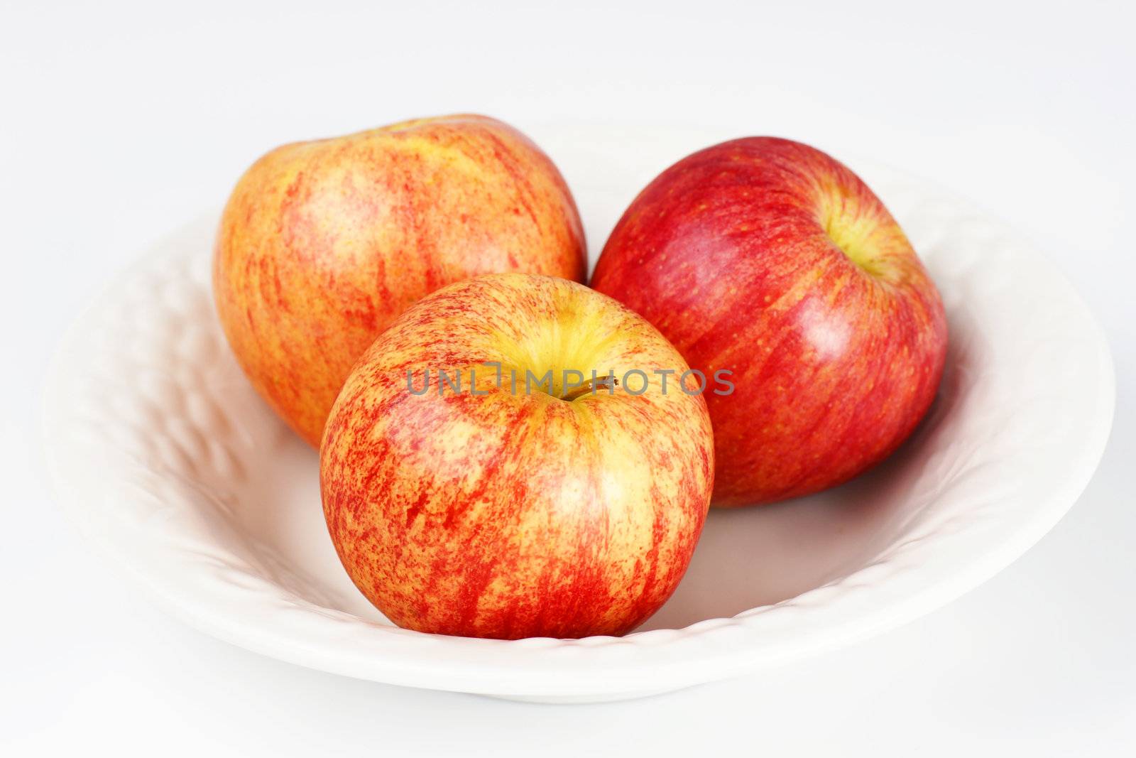 Clean and simple still life with three gala apples in a white porcelain bowl over white background.
