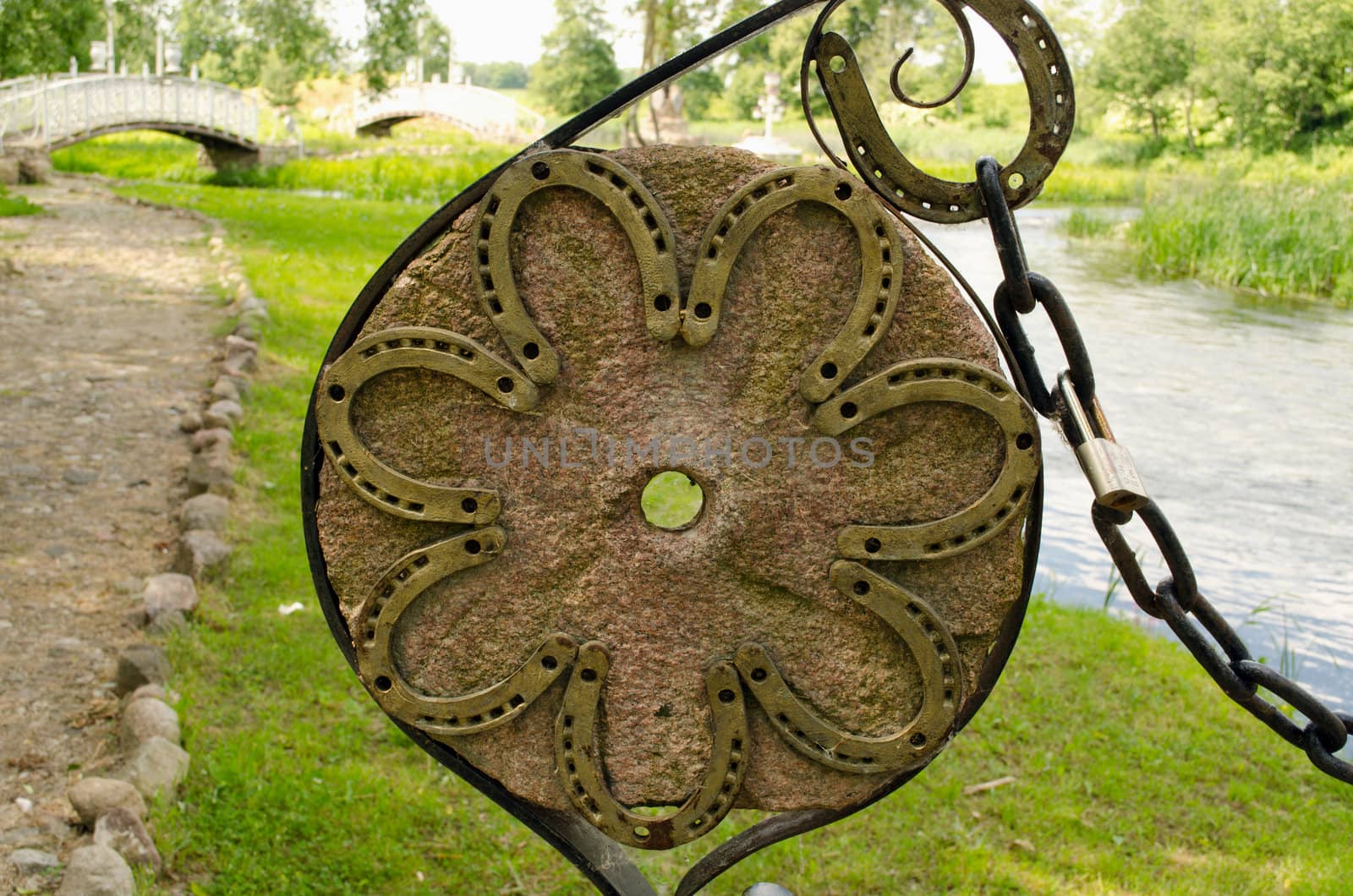 Horse shoes on old millstone and chain in park and nice white bridges in distance.