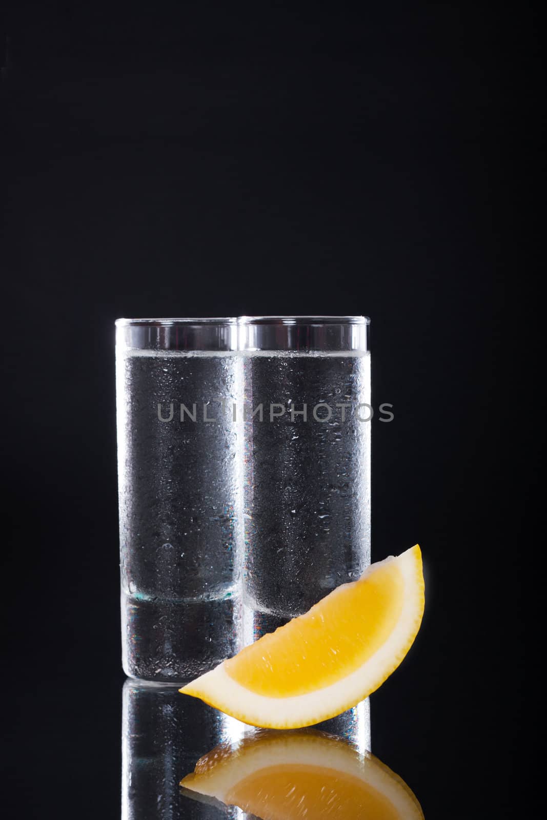 Shot glass filled with clear alcohol on a black background
